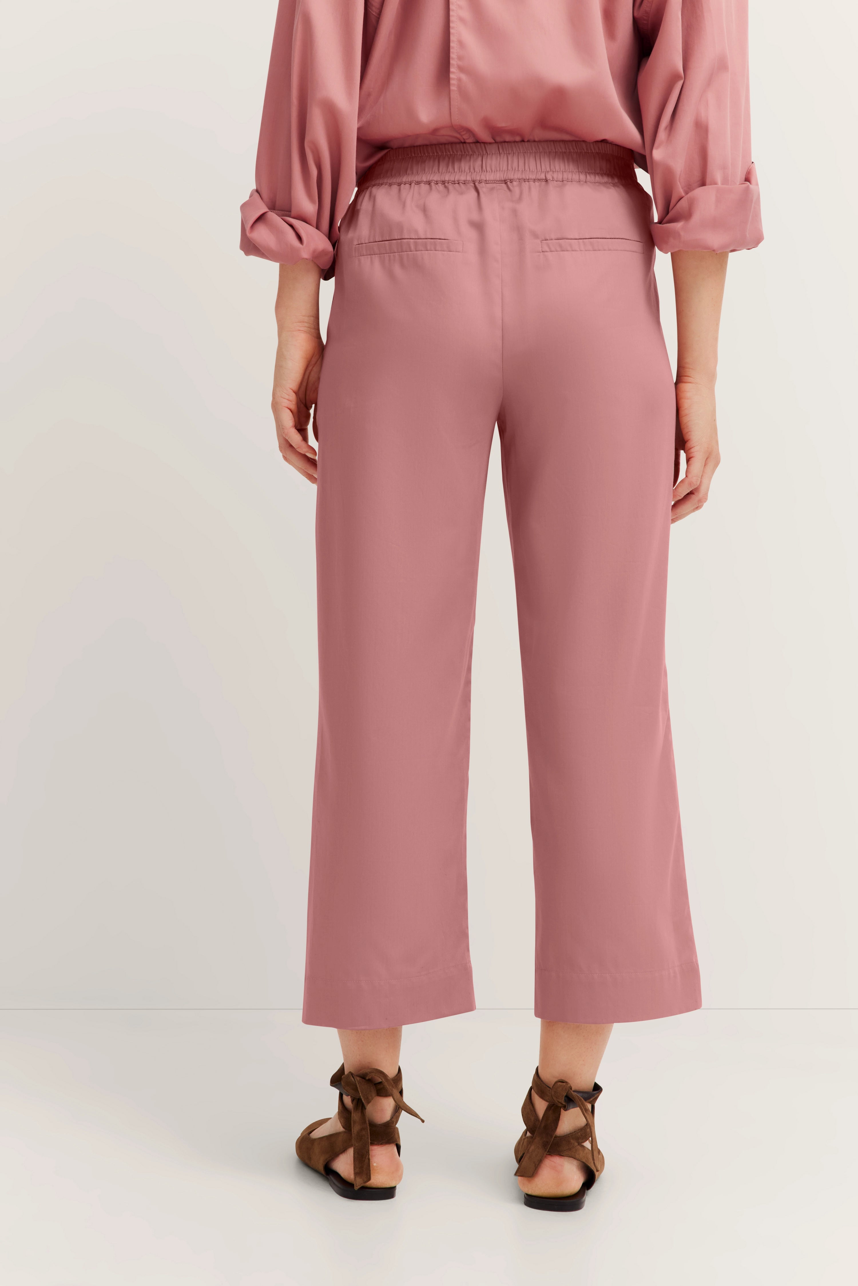 Achteraanzicht model in roze outfit, wijde broek, lange mouwen, casual, met sandalen.