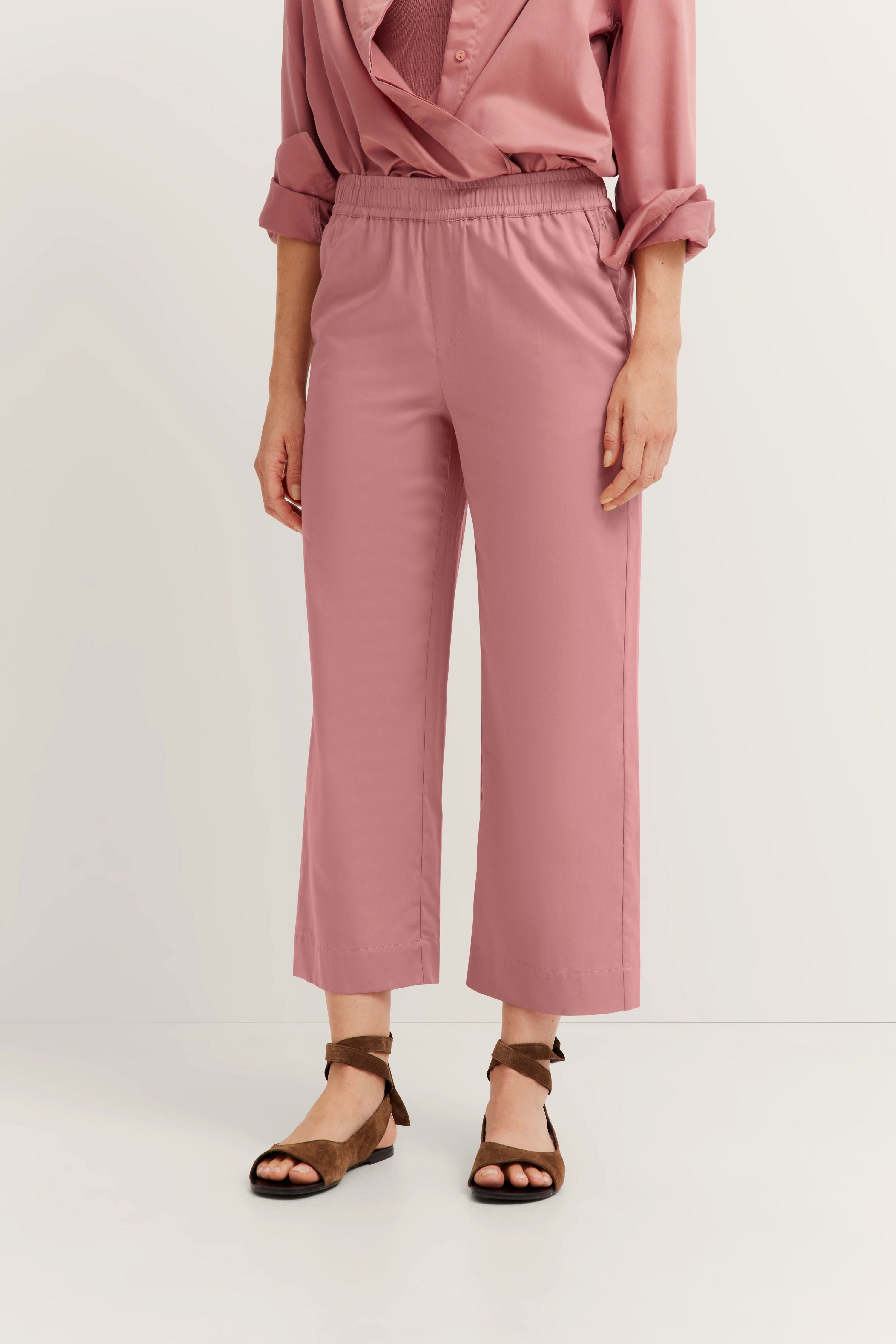 Roze ensemble met blouse en broek, casual modelbeeld, ontspannen pose.