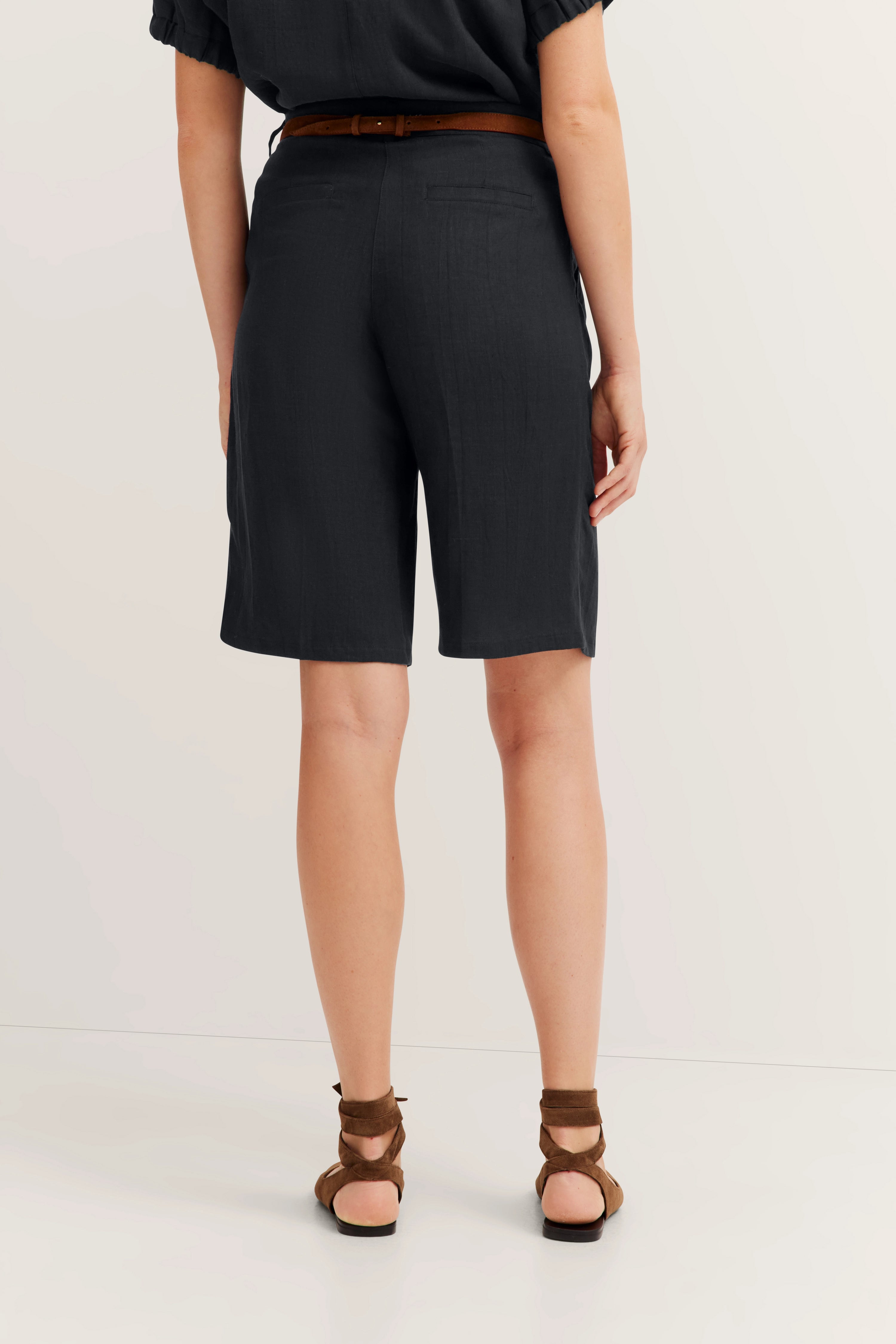 Schwarze bugatti Bermuda-Shorts, lockeres Modelbild, Rückansicht, kombiniert mit braunen Sandalen.