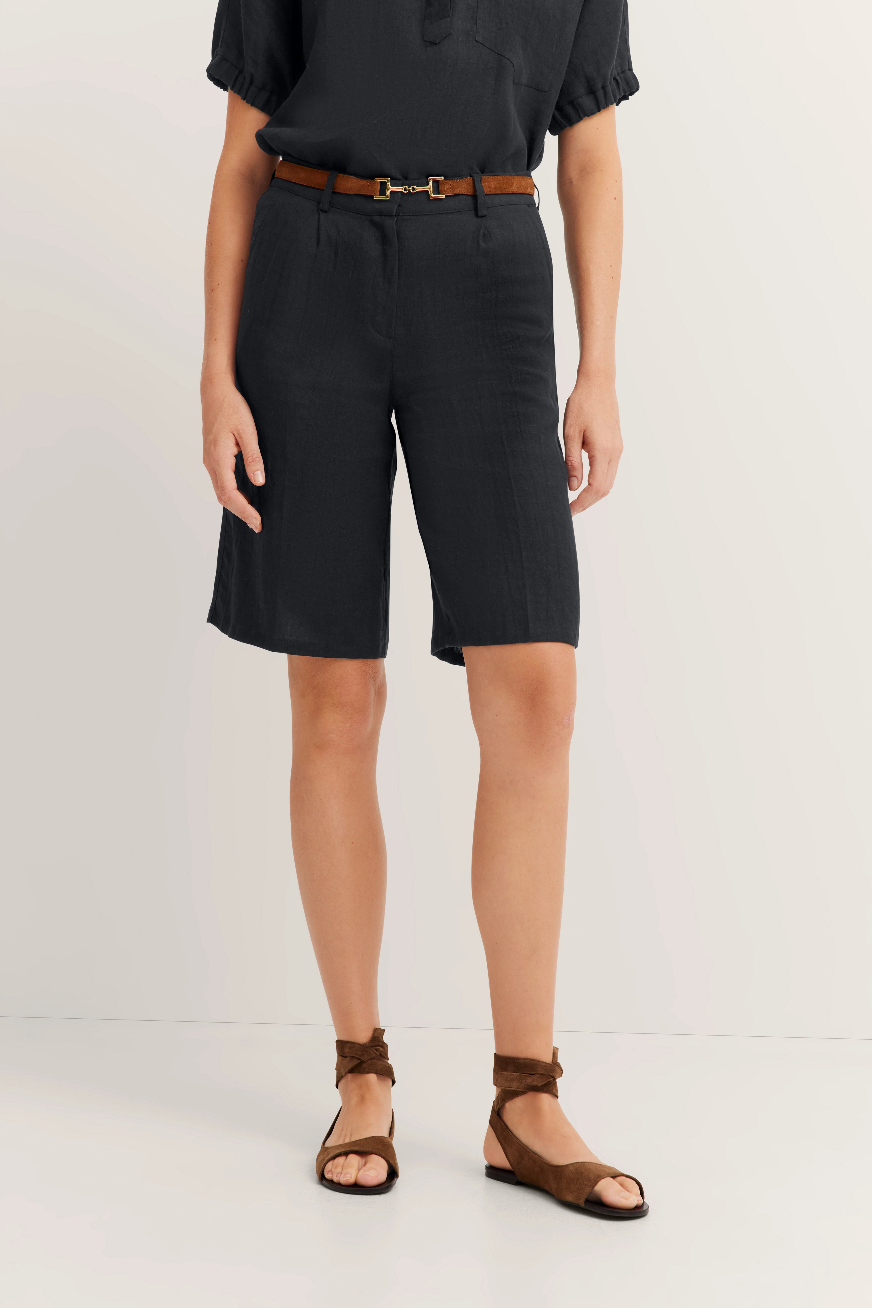 Schwarze Shorts mit braunem Gürtel und Sandalen, legeres Modelbild stehend.
