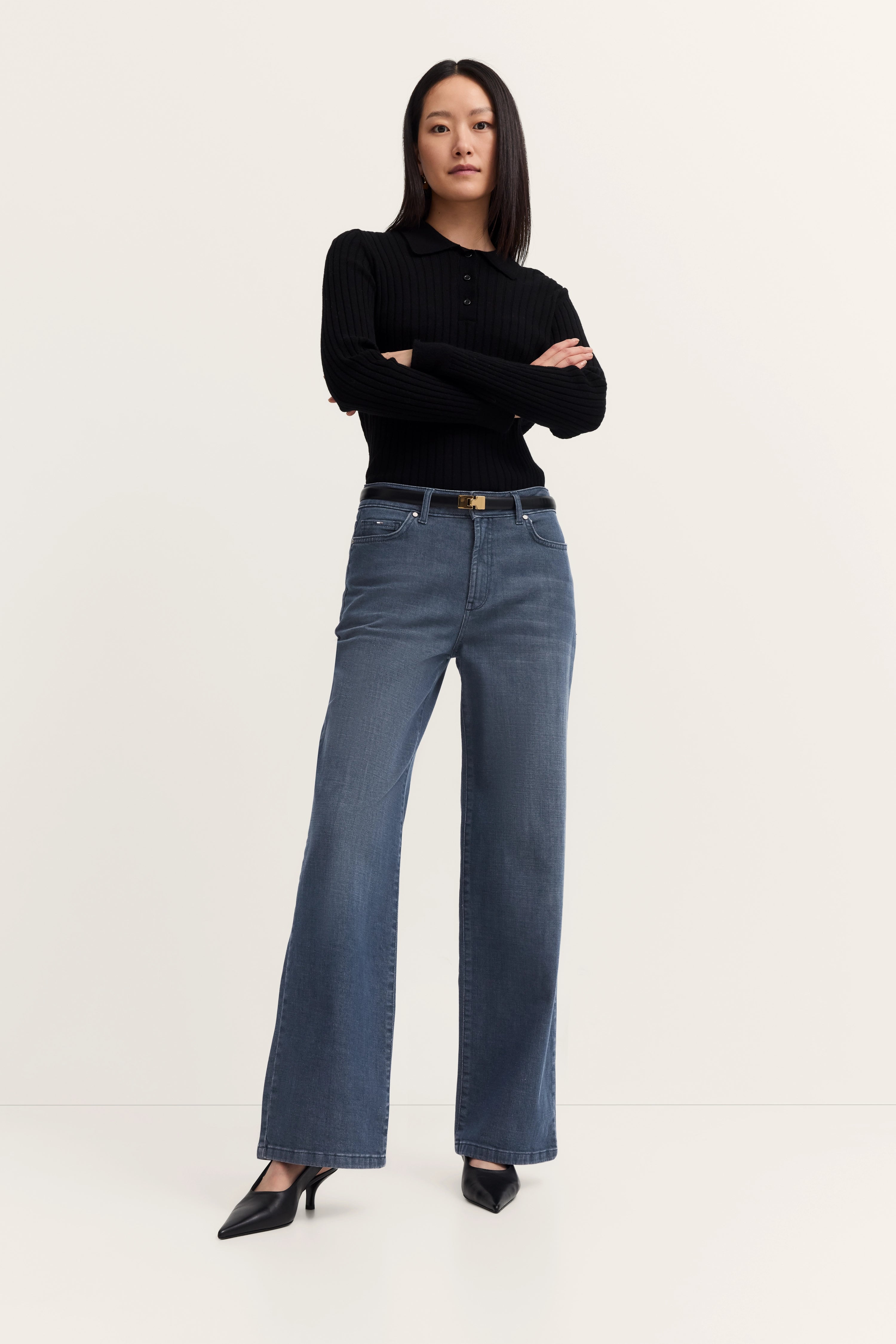"Model in schwarzem Pullover, blauer Jeans, schwarzer Absatz, Arme verschränkt, klassisch-elegant, bugatti."