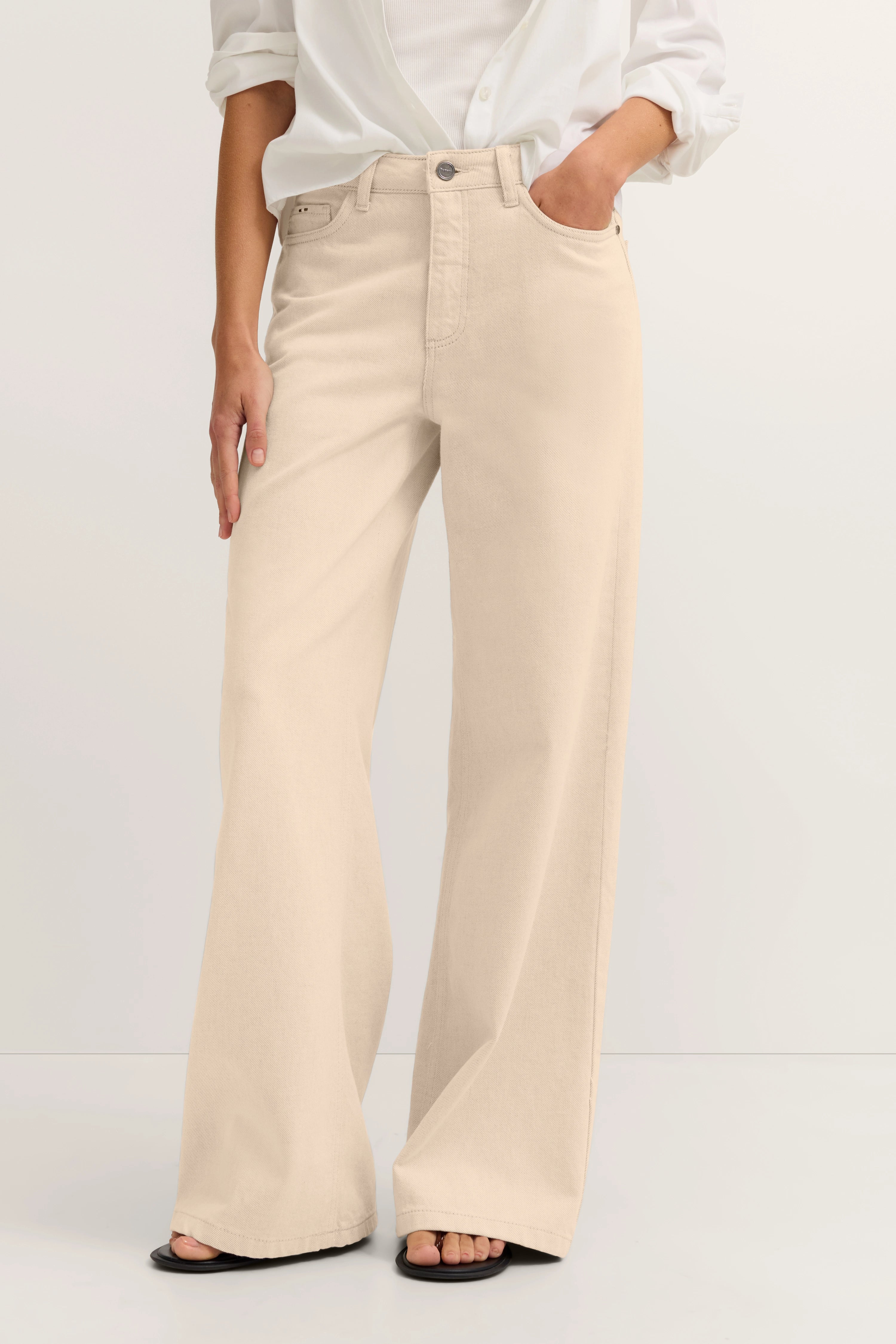 Beige weite Hose und weiße Bluse, legeres Modelbild, Hand in Tasche.