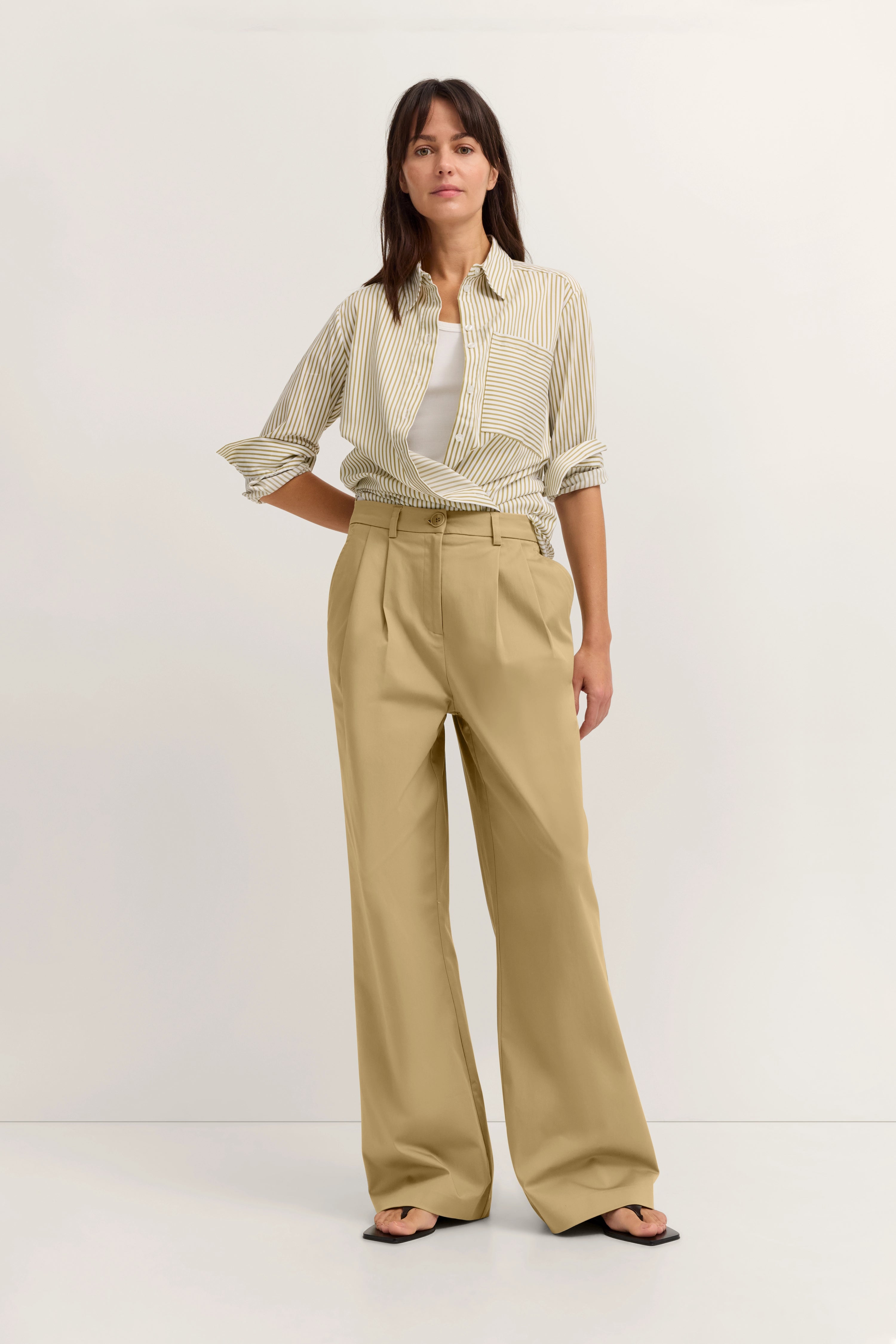 Model in beiger Hose, gestreiftem Hemd, weißem Top, lässige Pose.