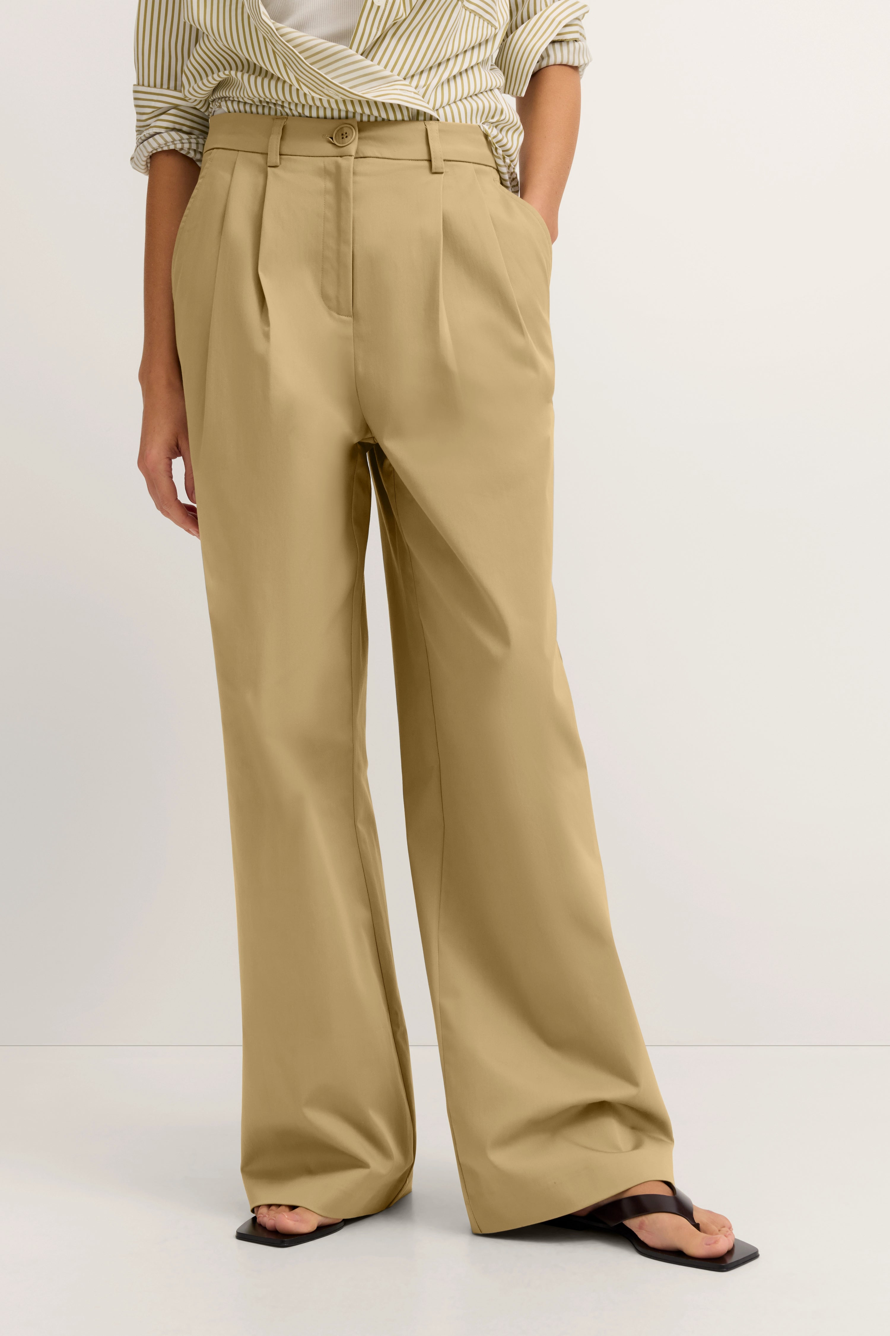 Beige weite Hose mit Streifenbluse, legeres Modelbild, entspannte Pose.