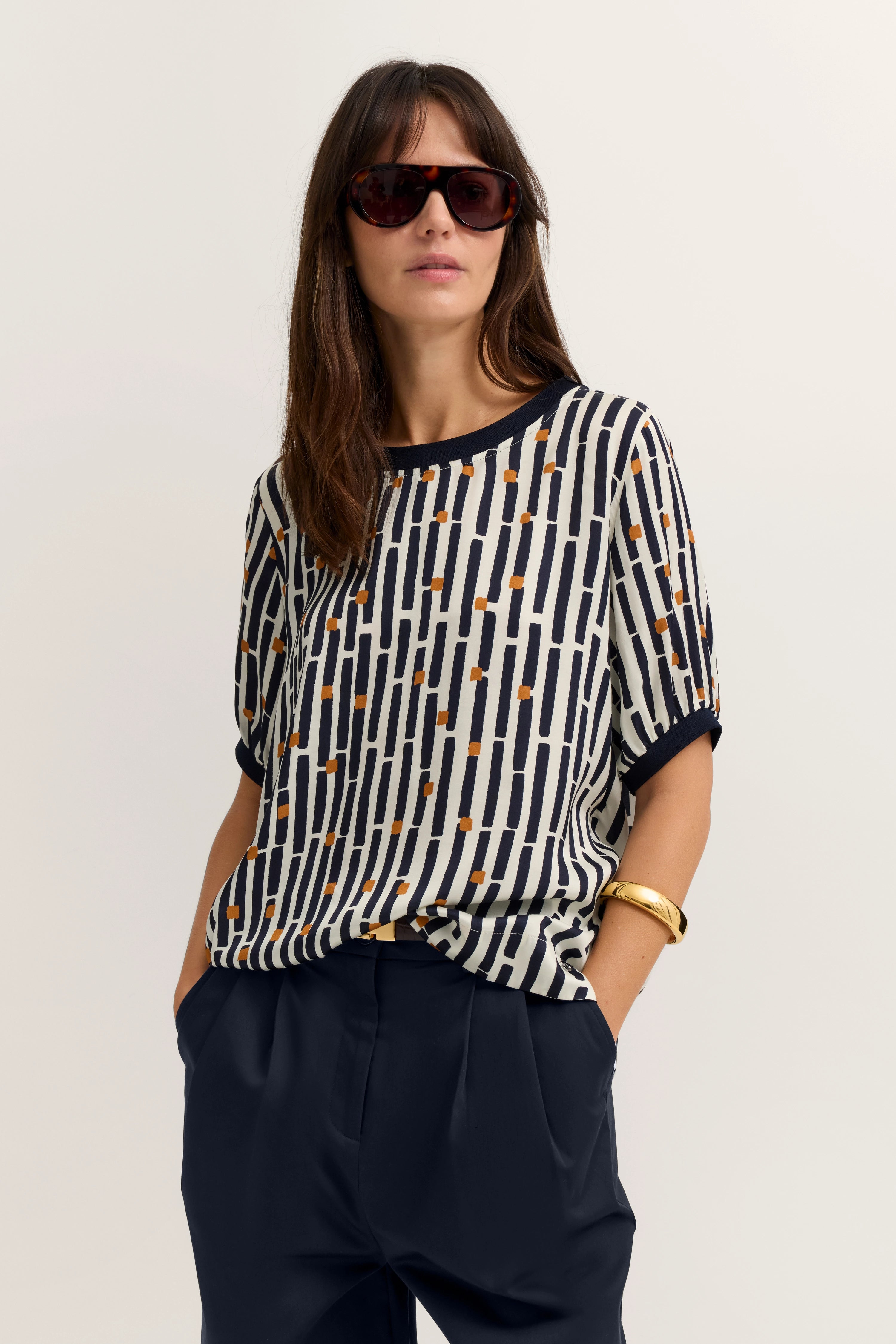 Modell in gemustertem bugatti Shirt mit dunkler Hose, lässige Pose, Sonnenbrille, stilvoll.