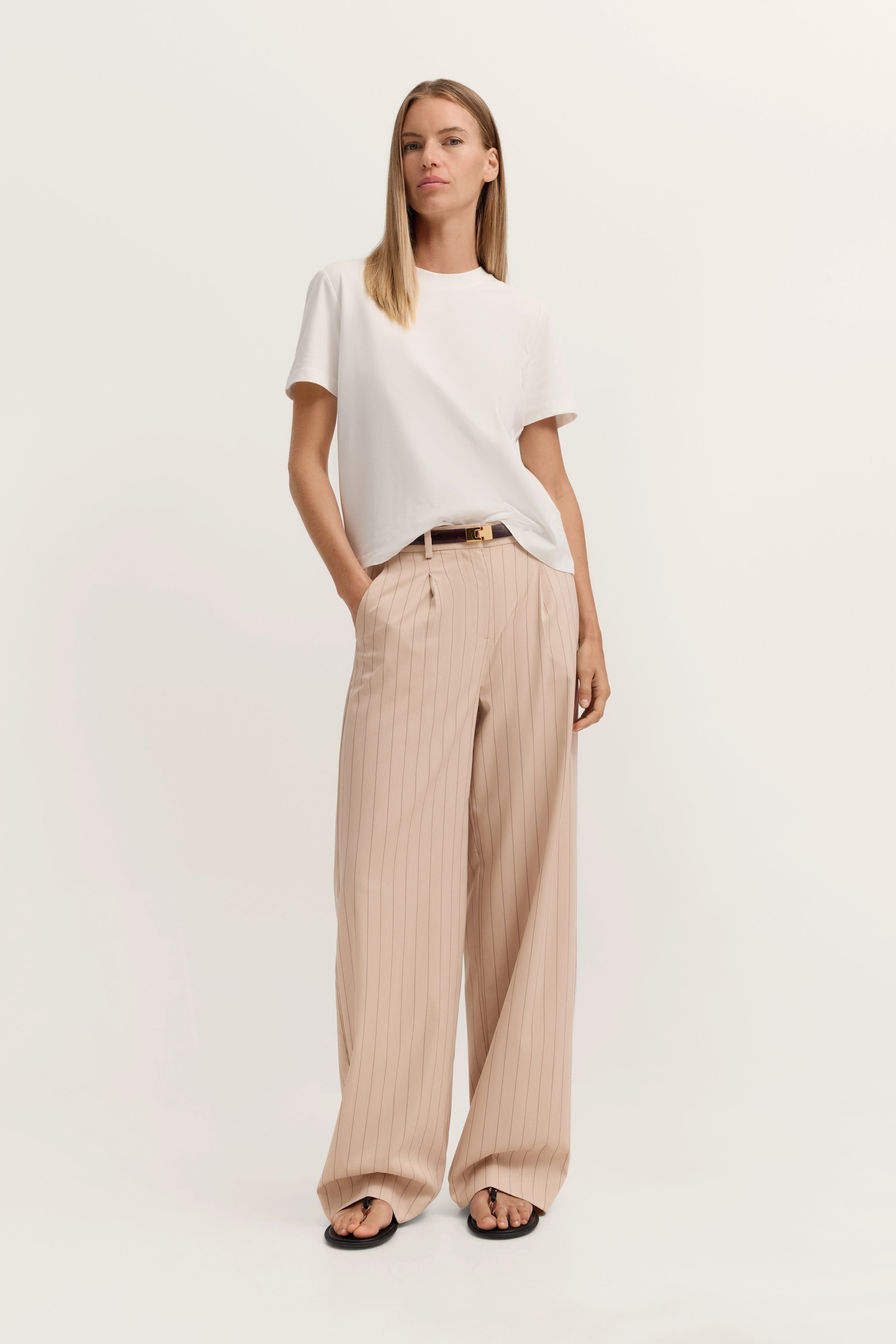 Weißes T-Shirt und beige gestreifte Hose, Model mit lockerer Pose, bugatti Stil.