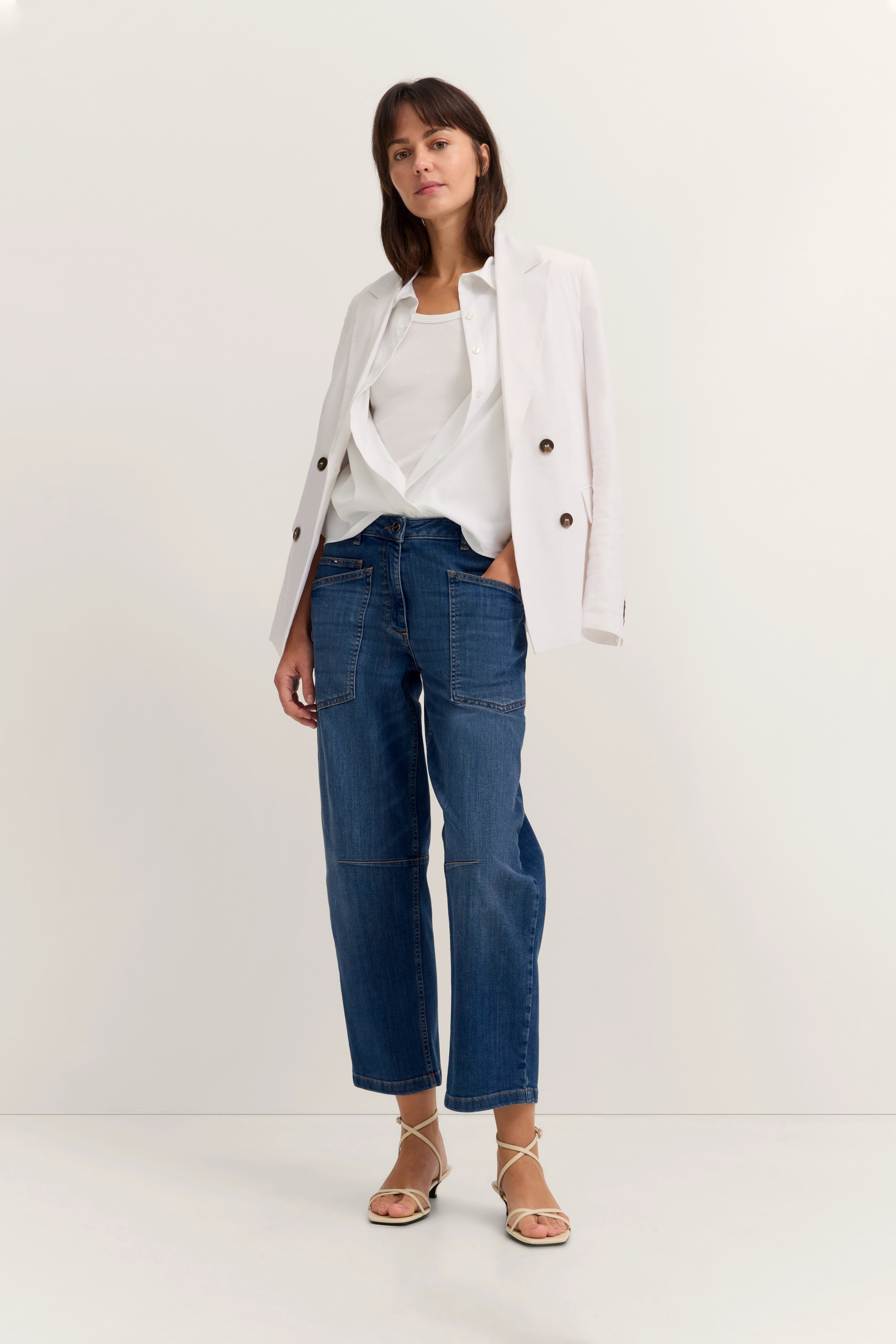 Model in weißem Blazer, weißem Top, blauer Jeans, legeres Pose