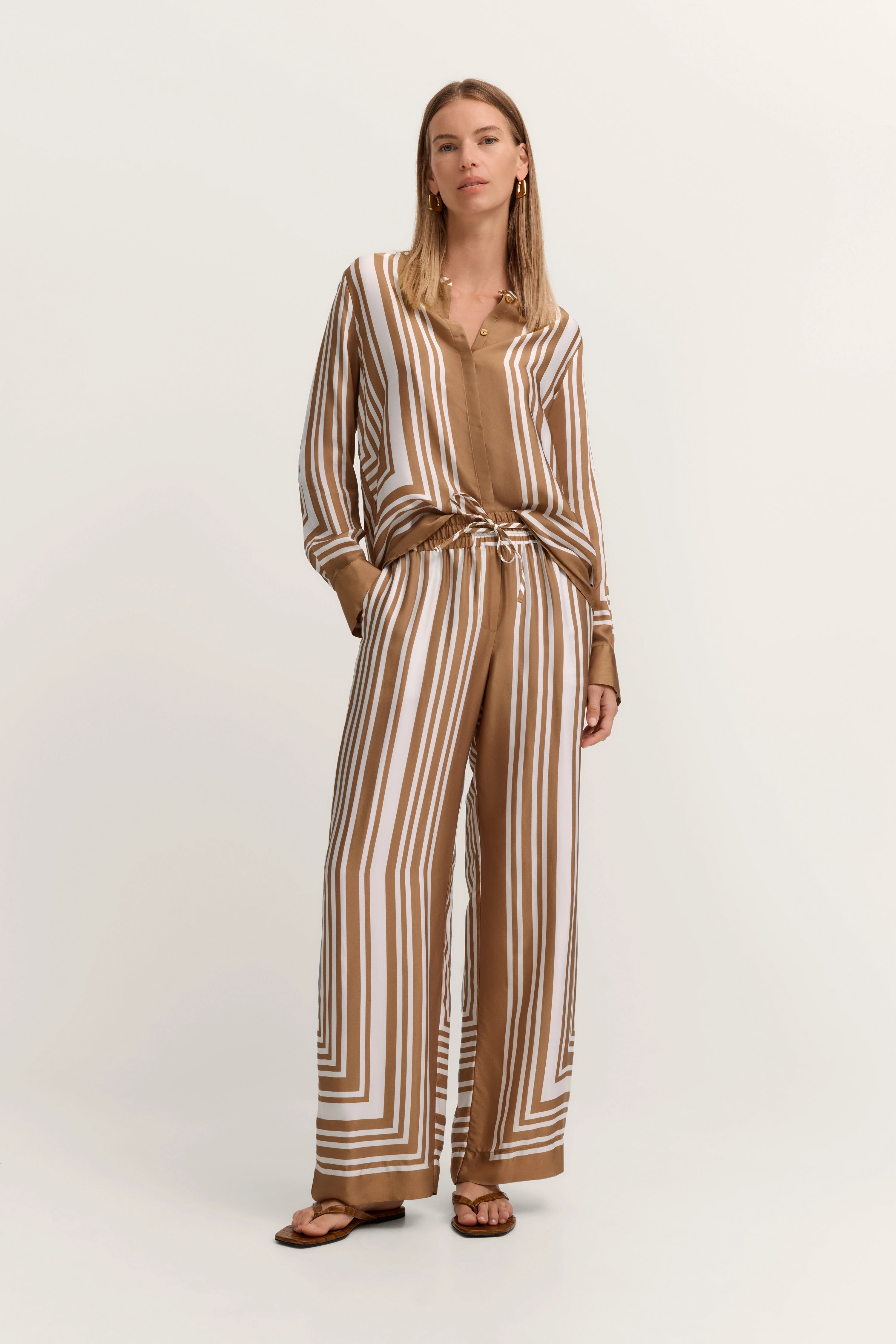 Model in gestreiftem, braun-weißem bugatti Outfit, lässig stehend, mit einem Hauch von Eleganz.