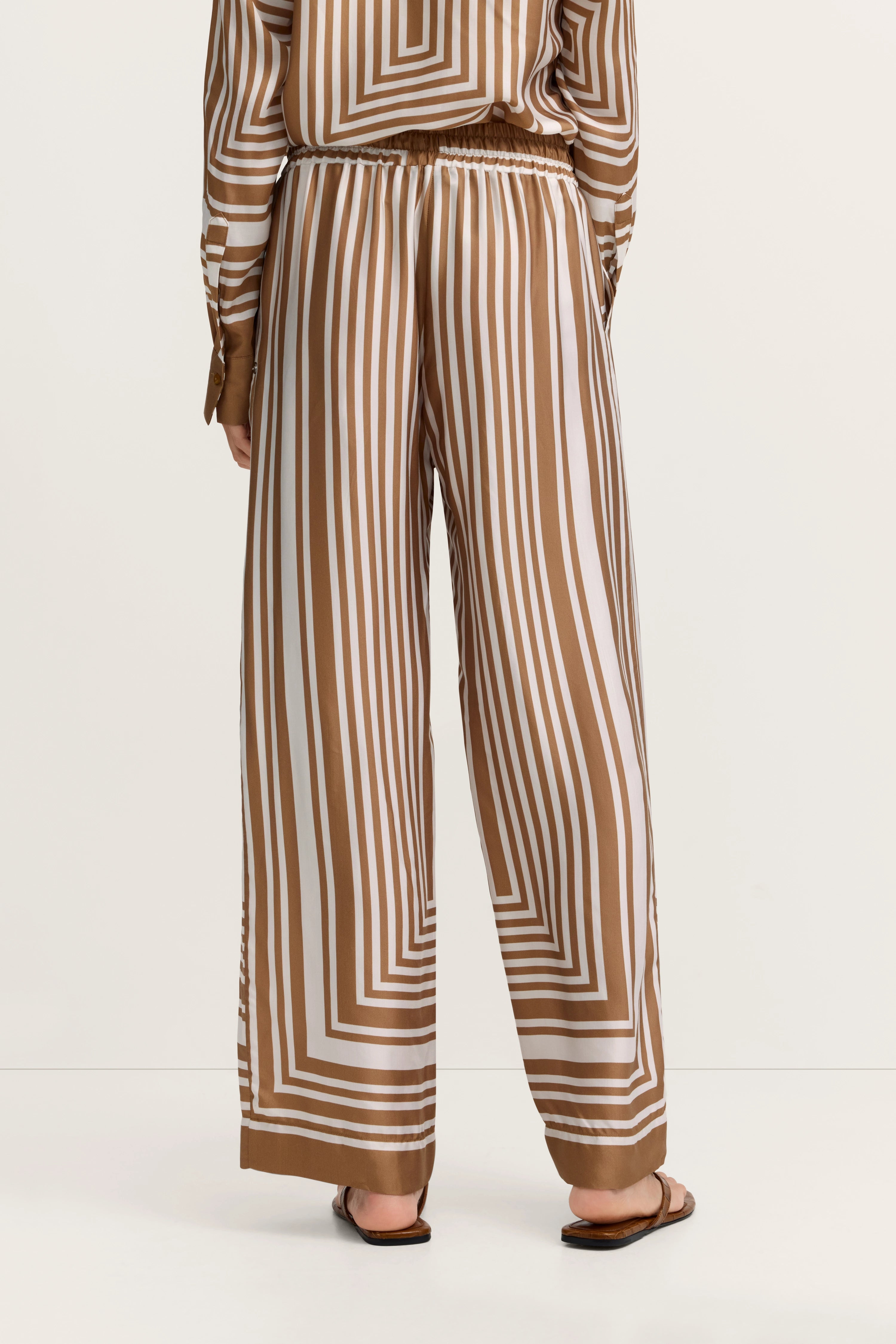 Weite Hose mit braun-weißen Streifen, Model von hinten, entspannte Pose, bugatti Stil.