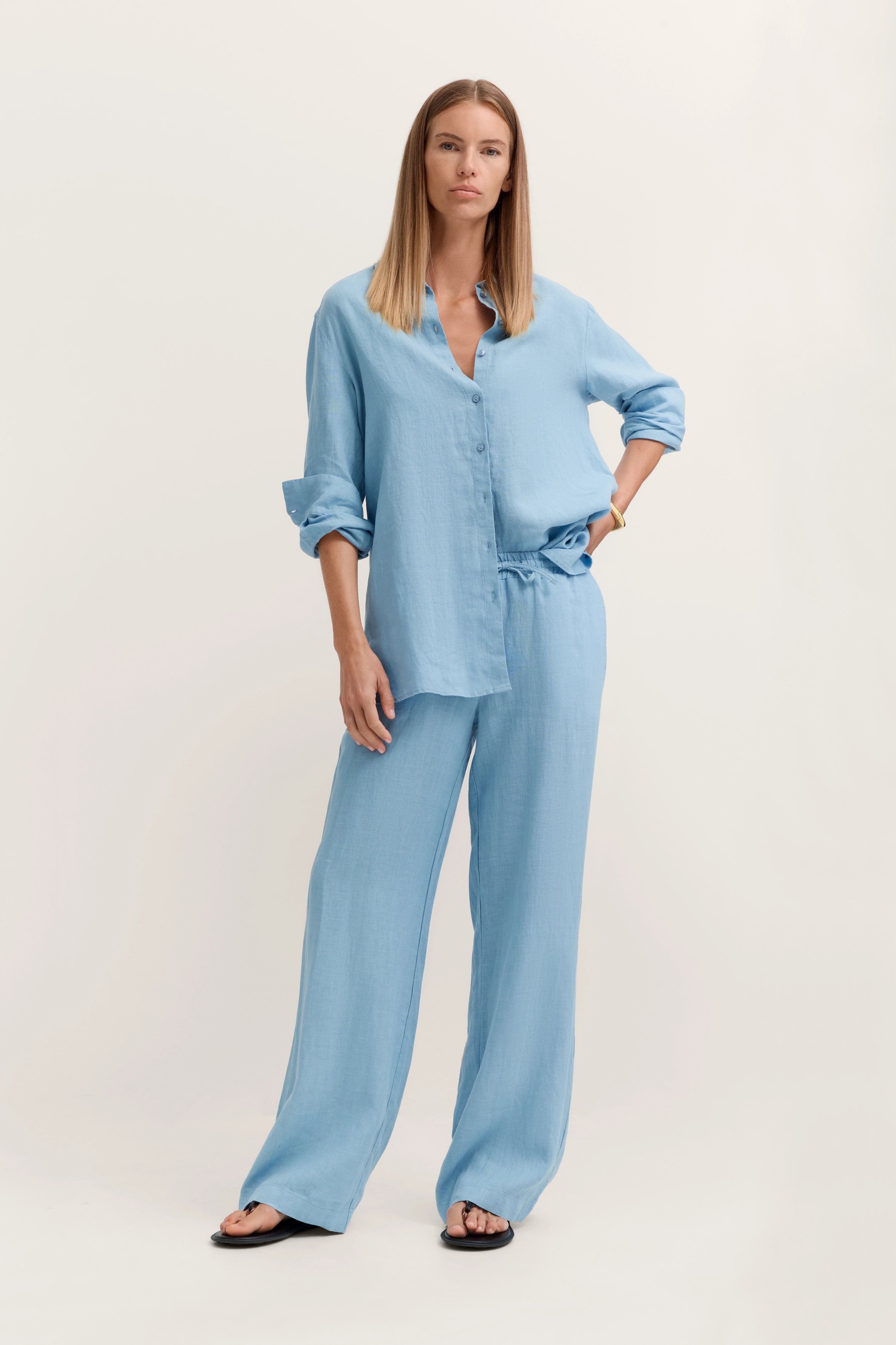 Blaues Set aus lockerem Hemd und weiten Hosen, Model posiert mit Hand in der Hüfte.
