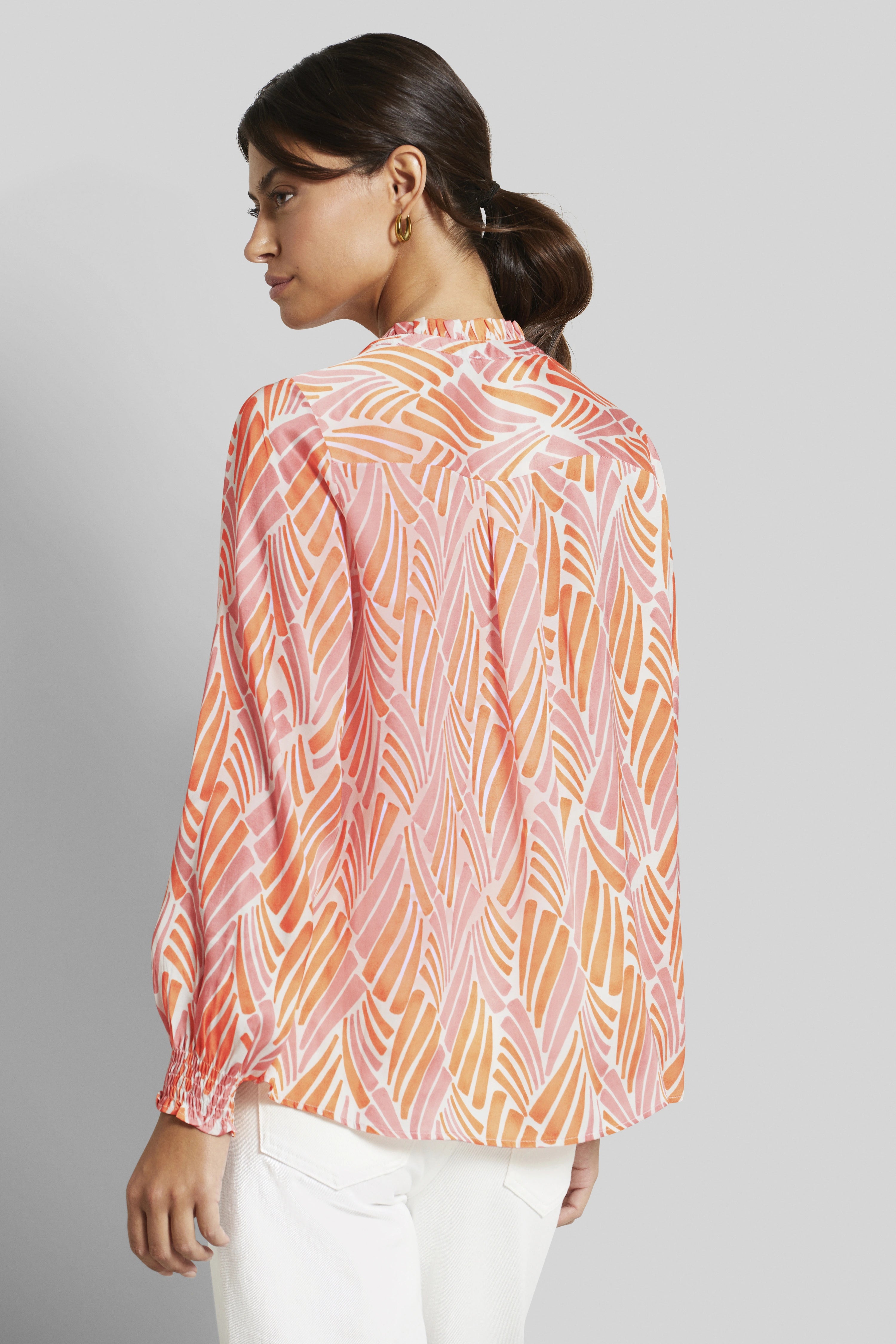 Modelbild mit bugatti Bluse in Rosa und Orange, grafisches Muster, legeres Posing von hinten.