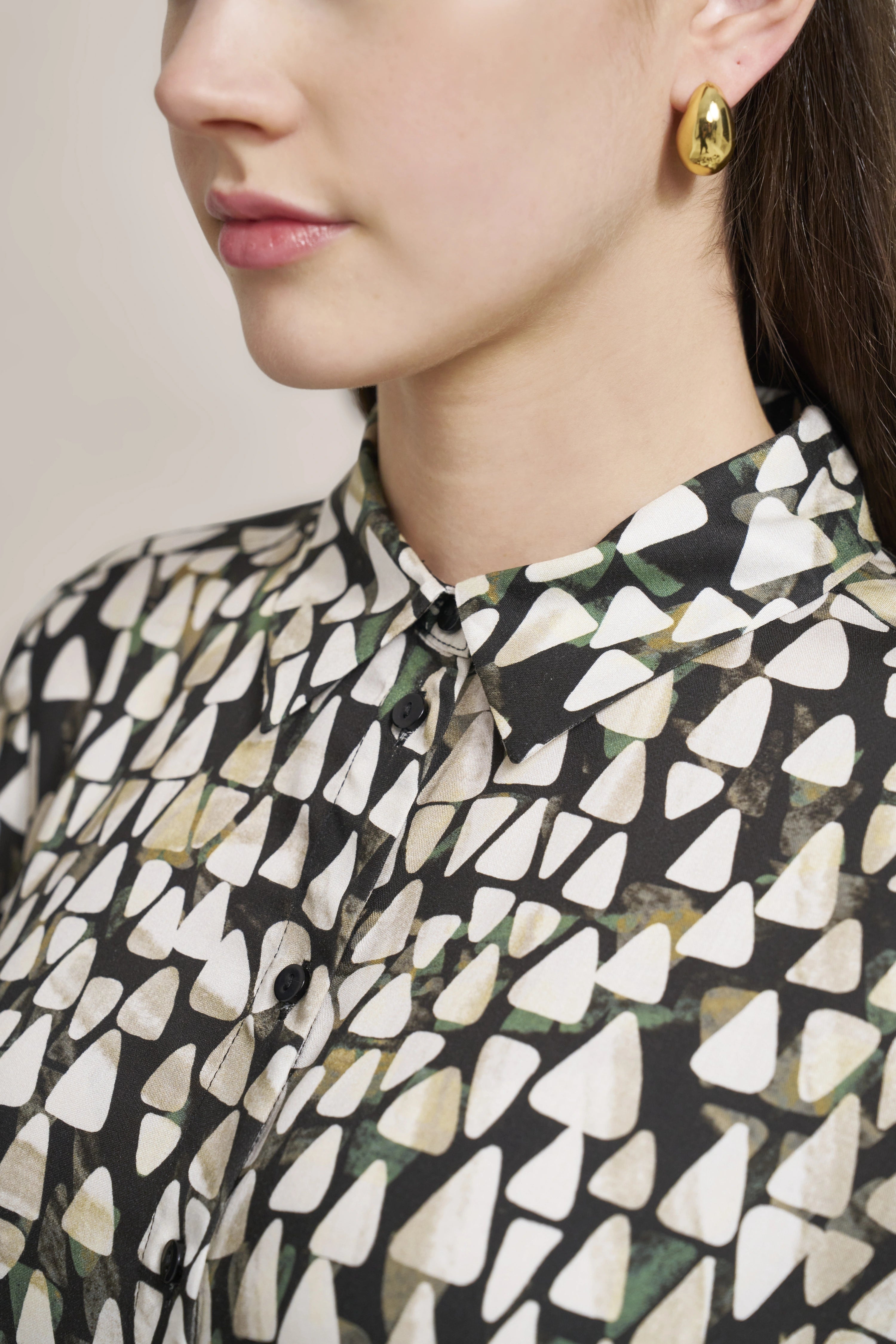 Bluse mit geometrischem Muster in Schwarz, Weiß und Grün, Büstenbild, goldene Ohrringe.