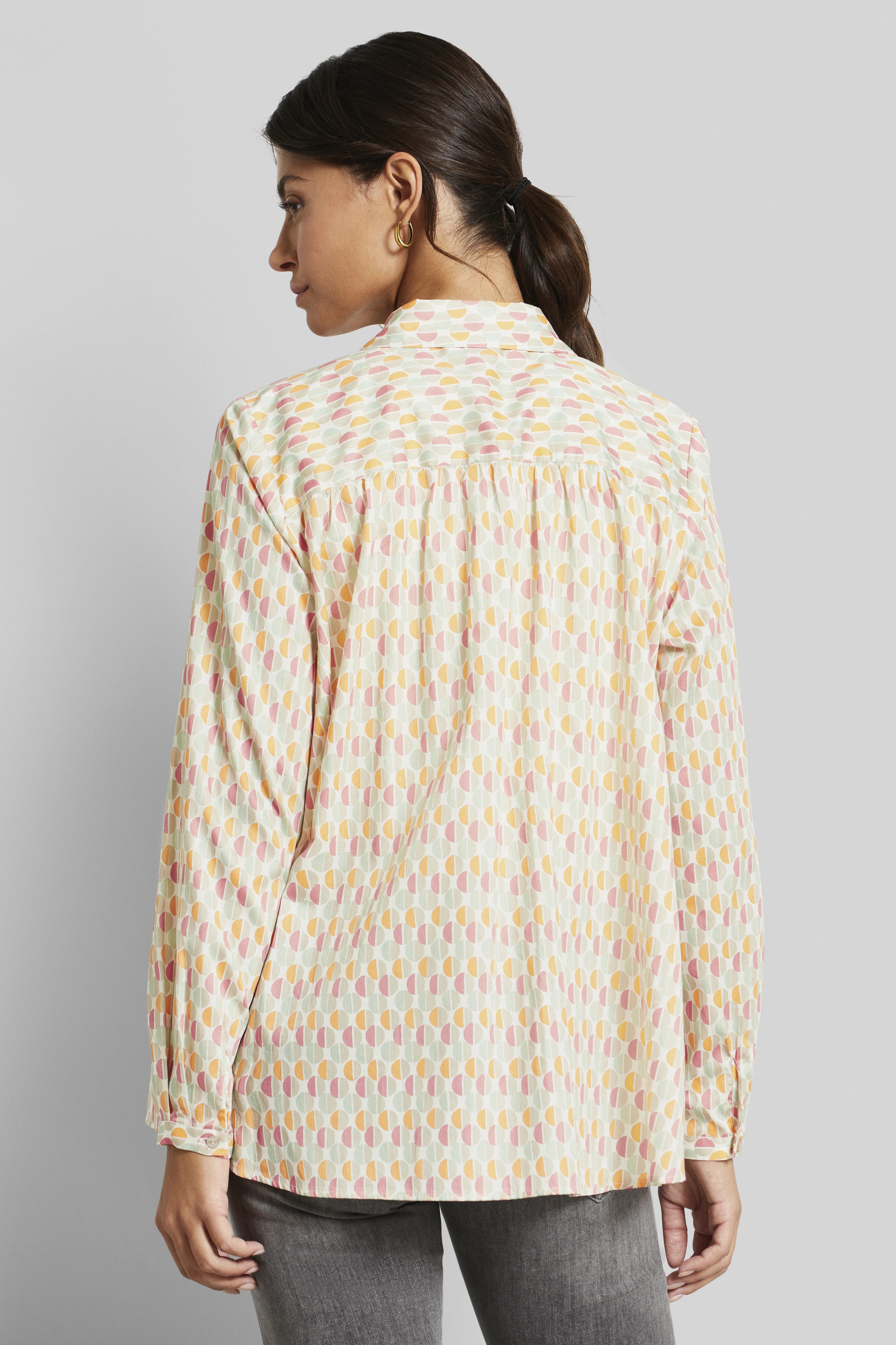 Bluse mit geometrischem Muster in Pastellfarben, Model von hinten, entspanntes Posing, bugatti Stil.