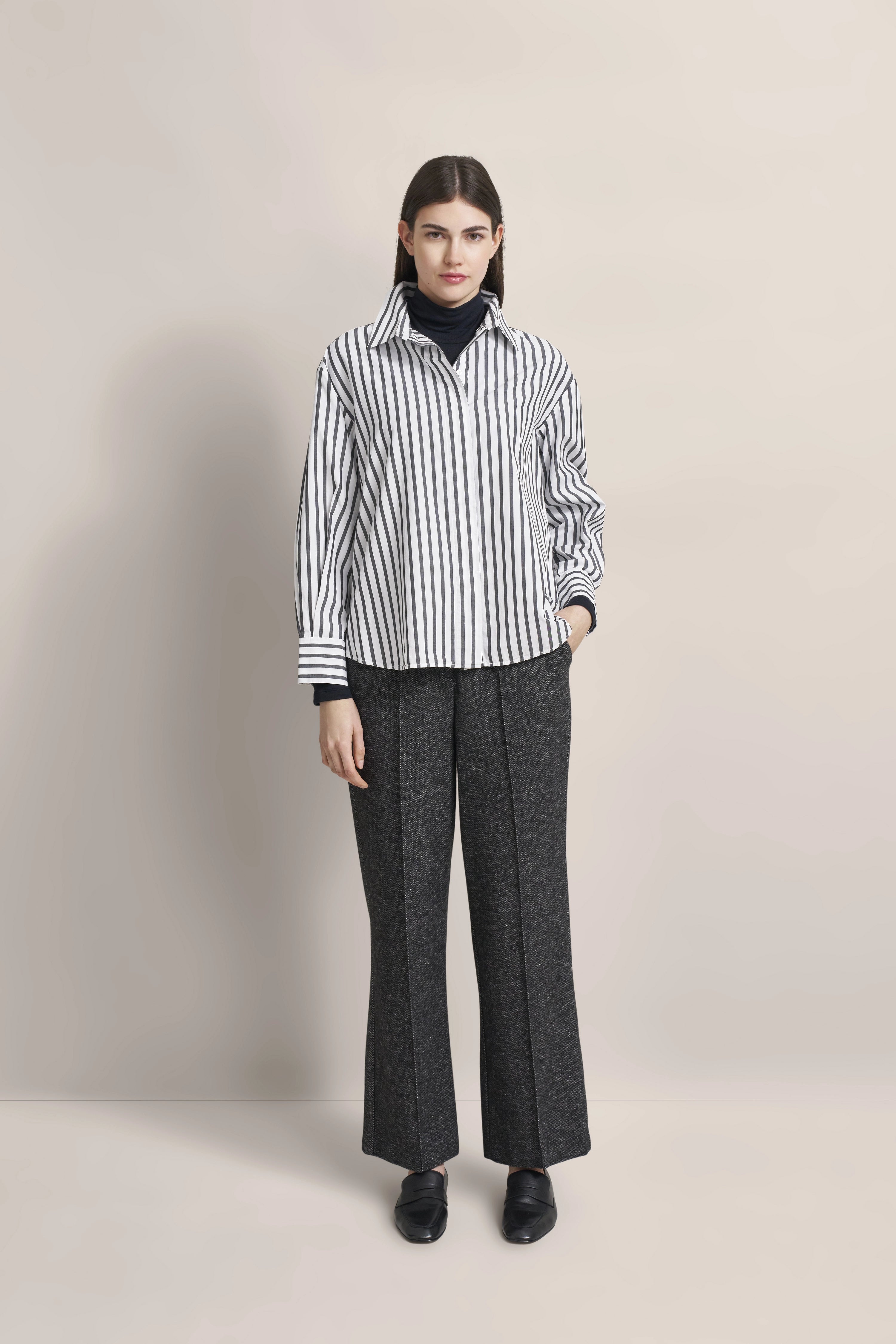 Model in striped bugatti blouse and gray pants, casual pose.