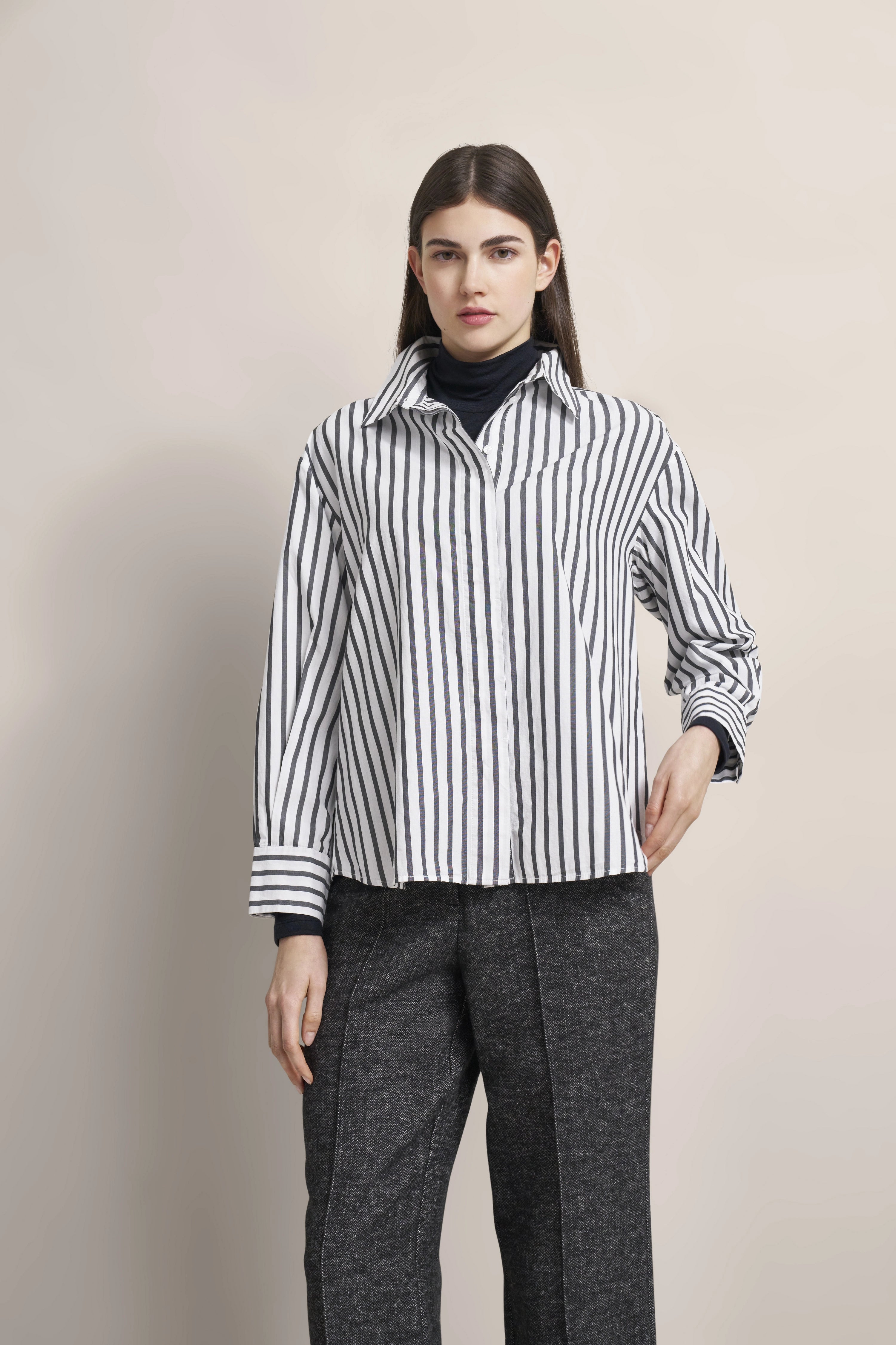 Schwarz-weiß gestreiftes Hemd, graue Hose, Modelbild, entspannte Haltung.