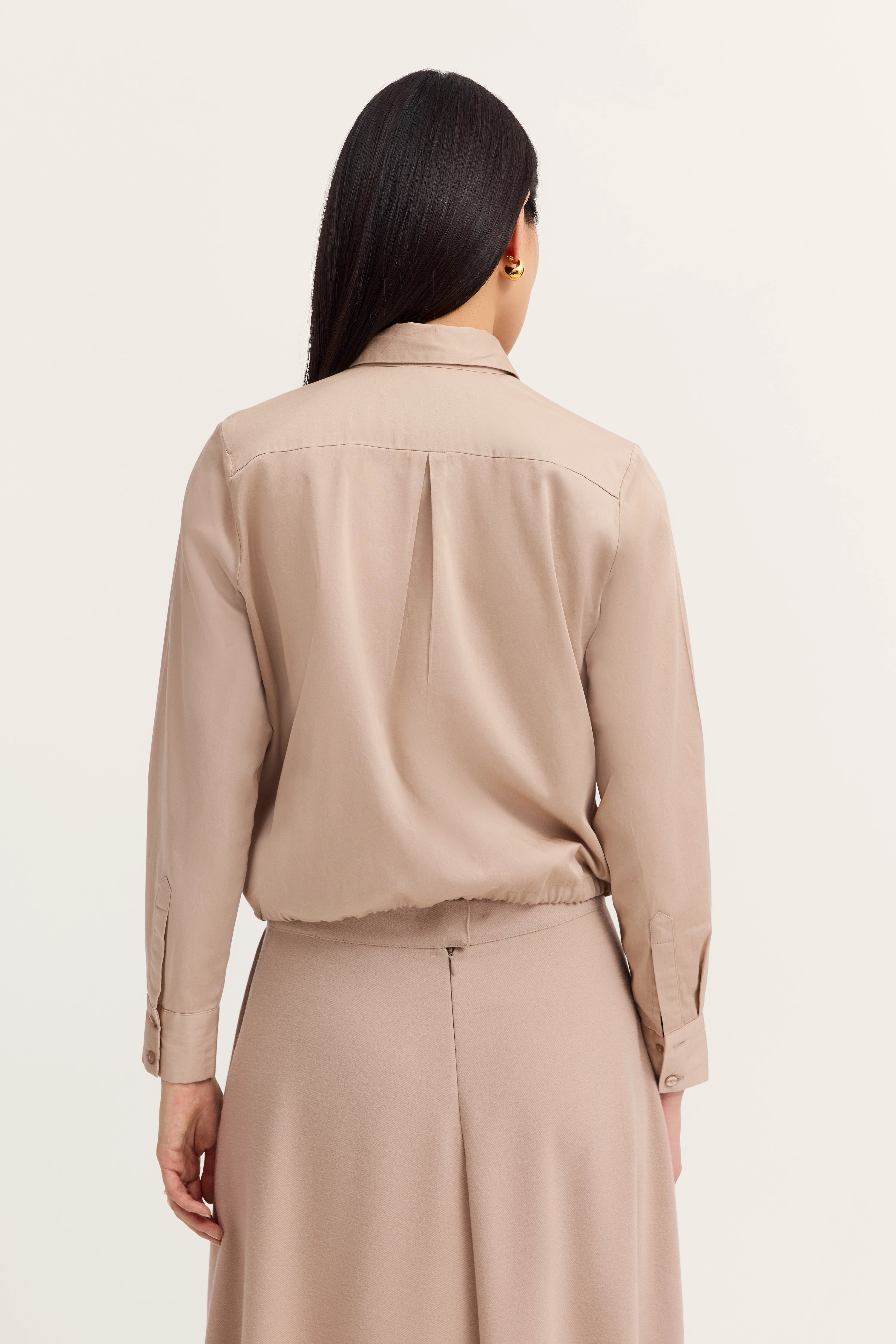 Beigefarbene Bluse und Rock von bugatti, Modelbild von hinten, entspanntes Posing.