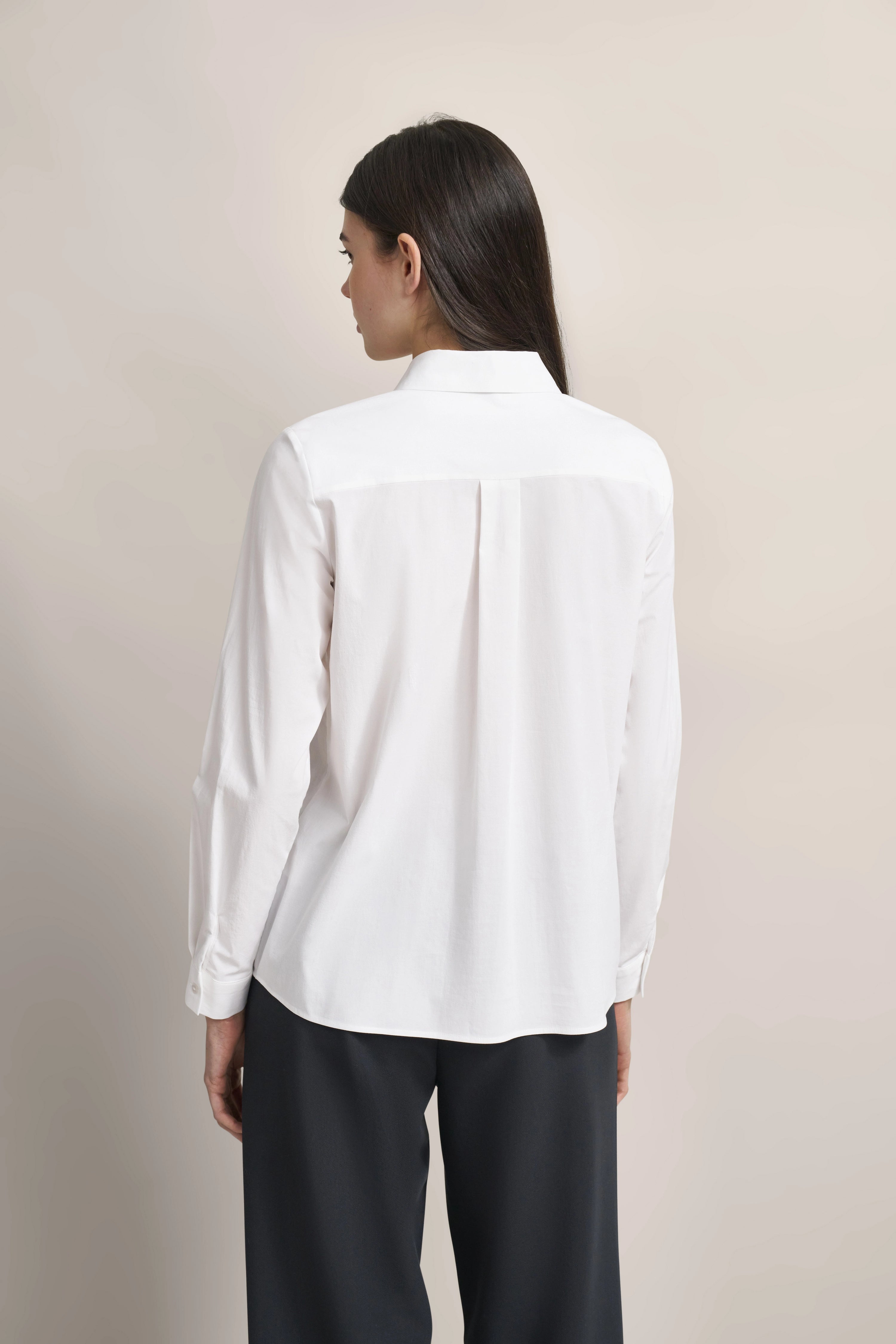 Weiße Bluse von bugatti, Modelbild, Rückansicht, entspanntes Posing, kombiniert mit schwarzen Hosen.
