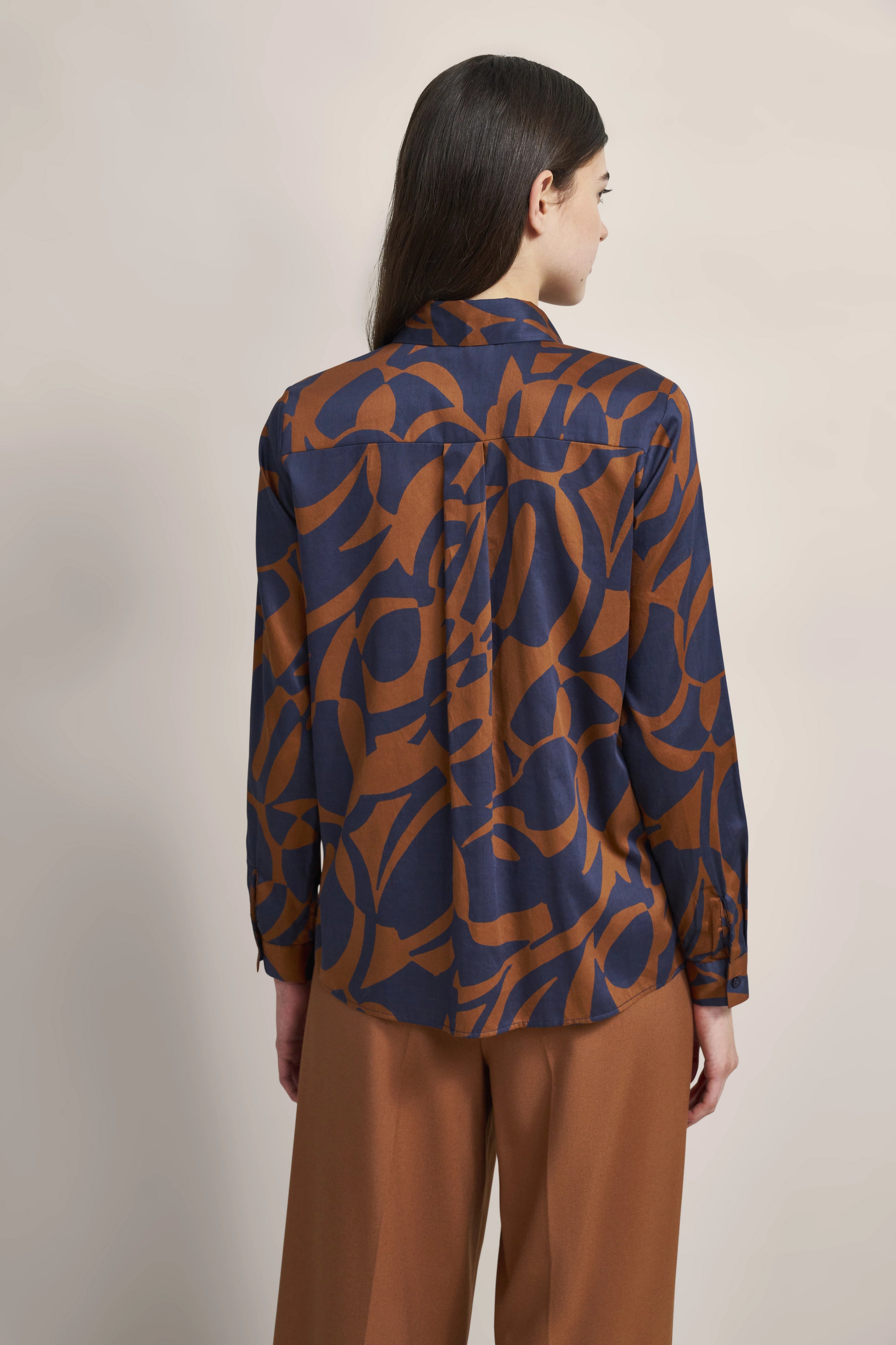 Bluse mit blau-braunem Muster, kombiniert mit brauner Hose, Modelbild von hinten, entspanntes Posing.