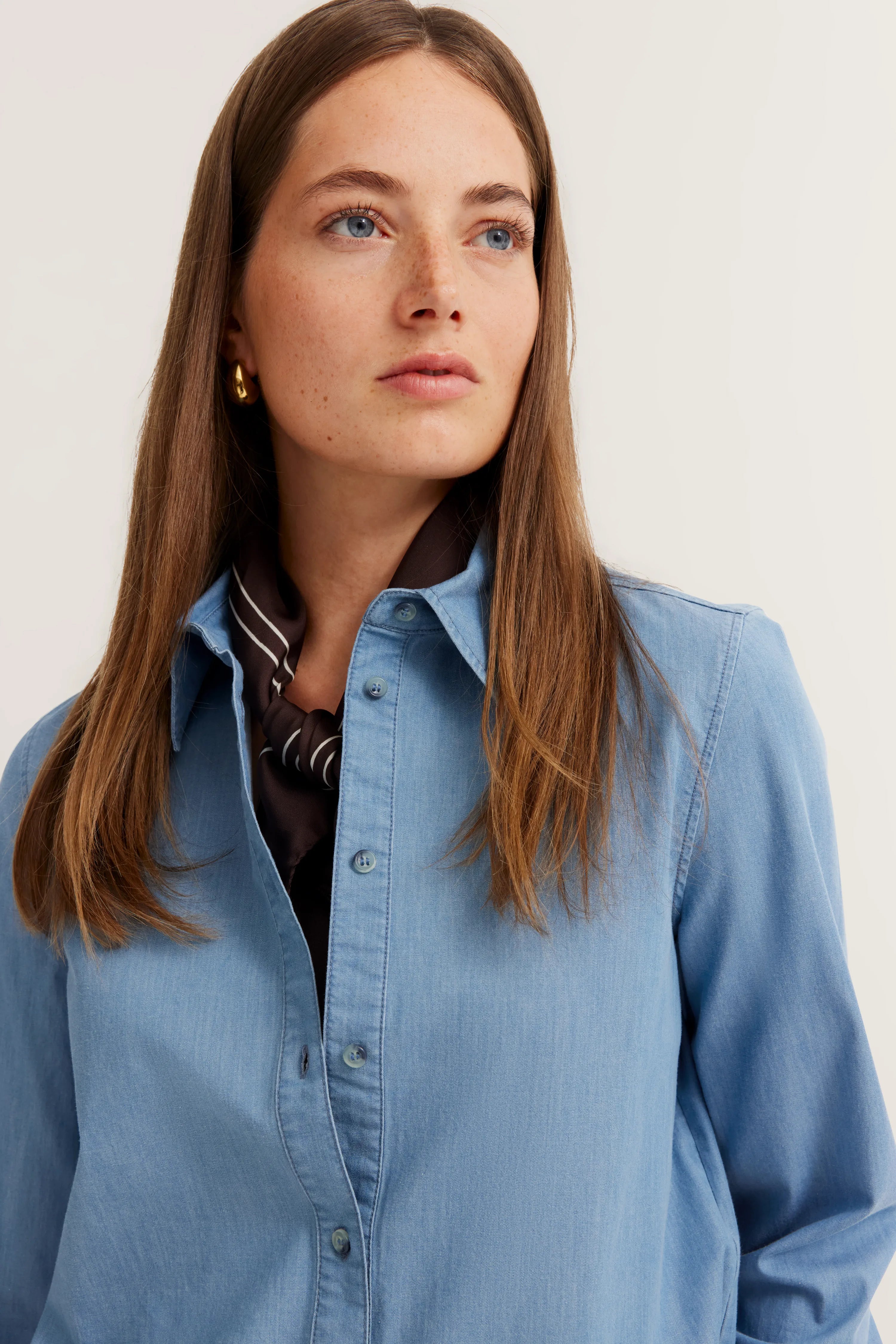 Blaues Denim-Hemd mit braunem Tuch, Modelbild, entspannter Blick zur Seite.