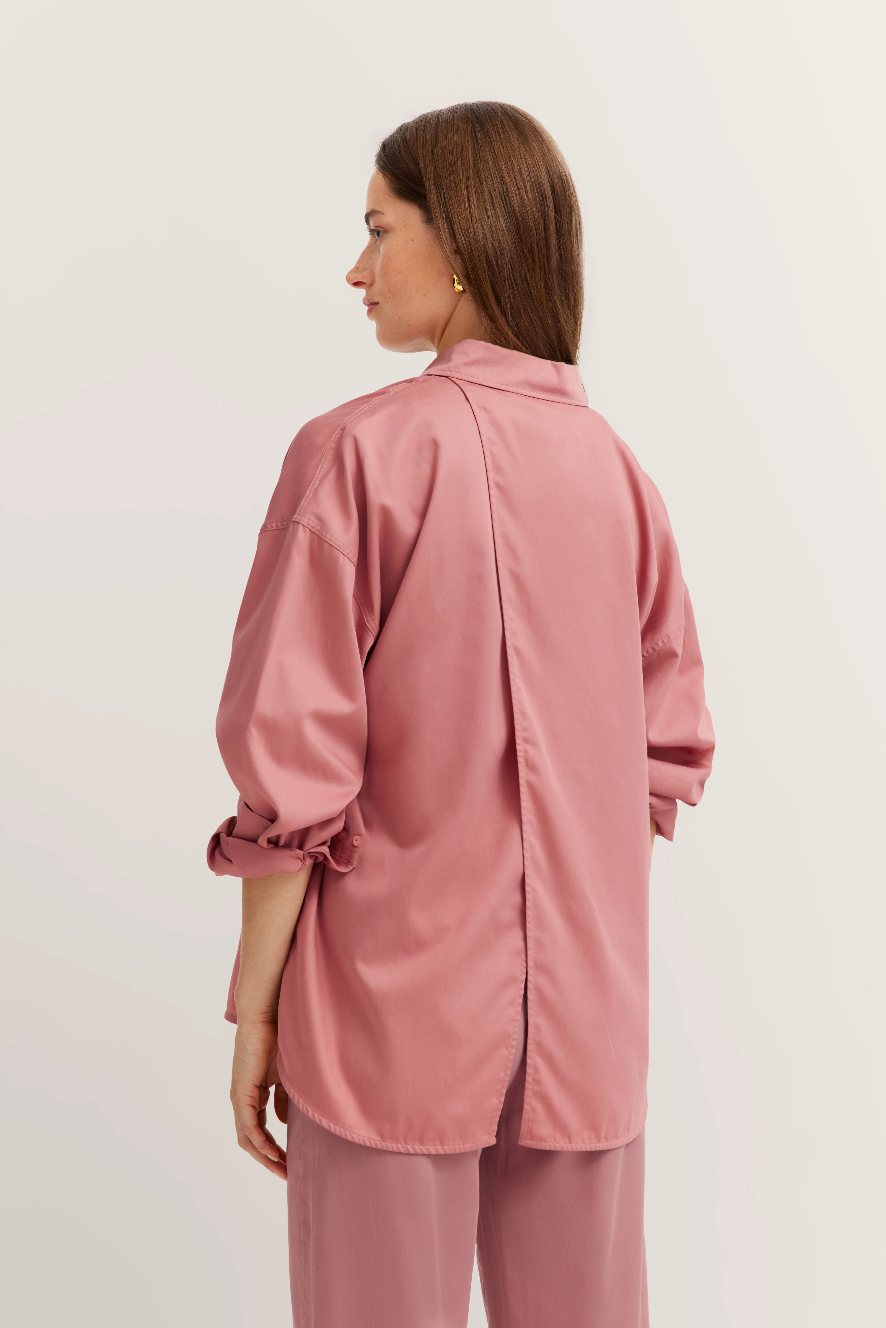 Rückenansicht Model in rosa Bluse und Hose, elegantes Design, lässige Pose.