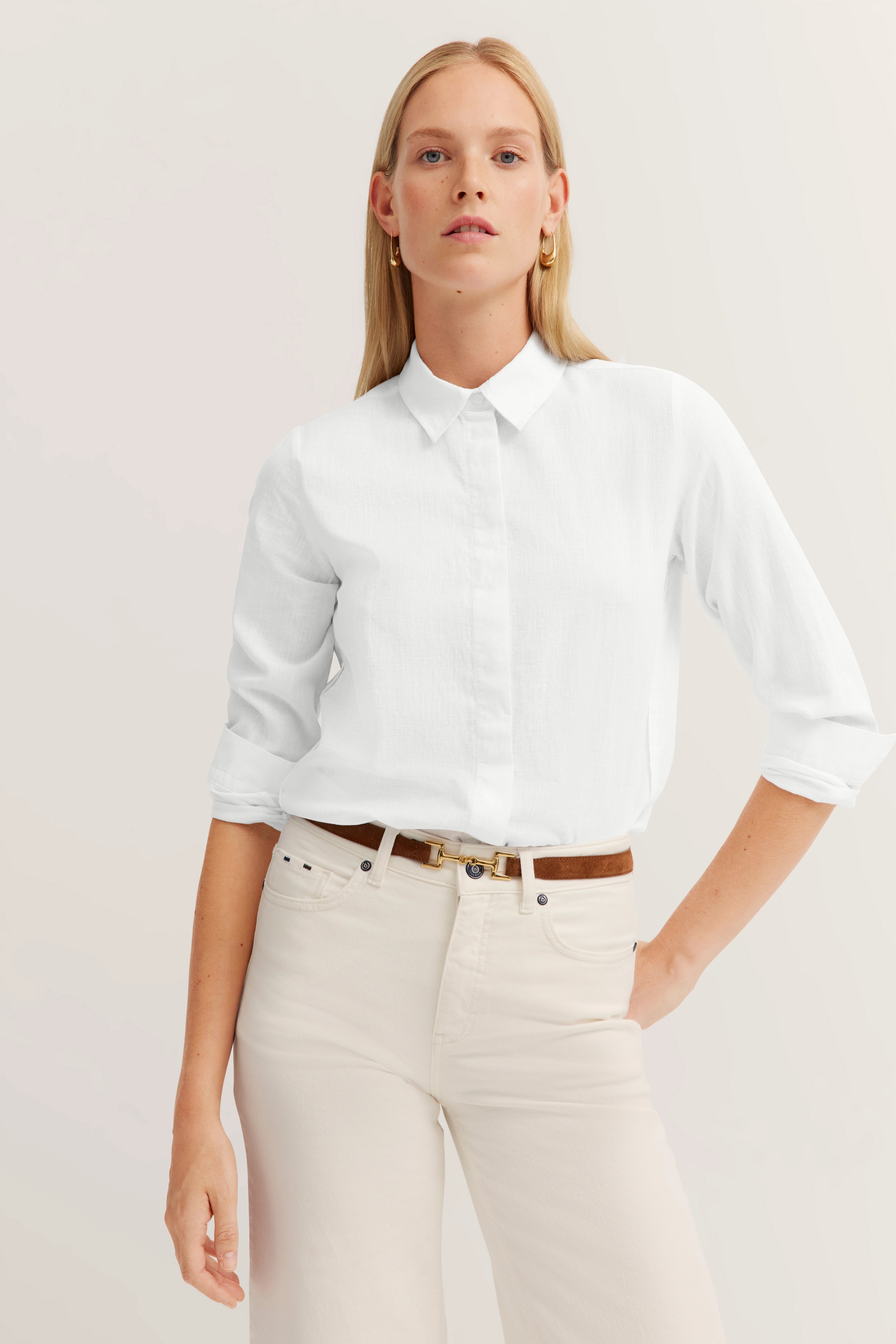 Weiße Bluse, beige Hose, brauner Gürtel, Modelbild, entspannte Pose.