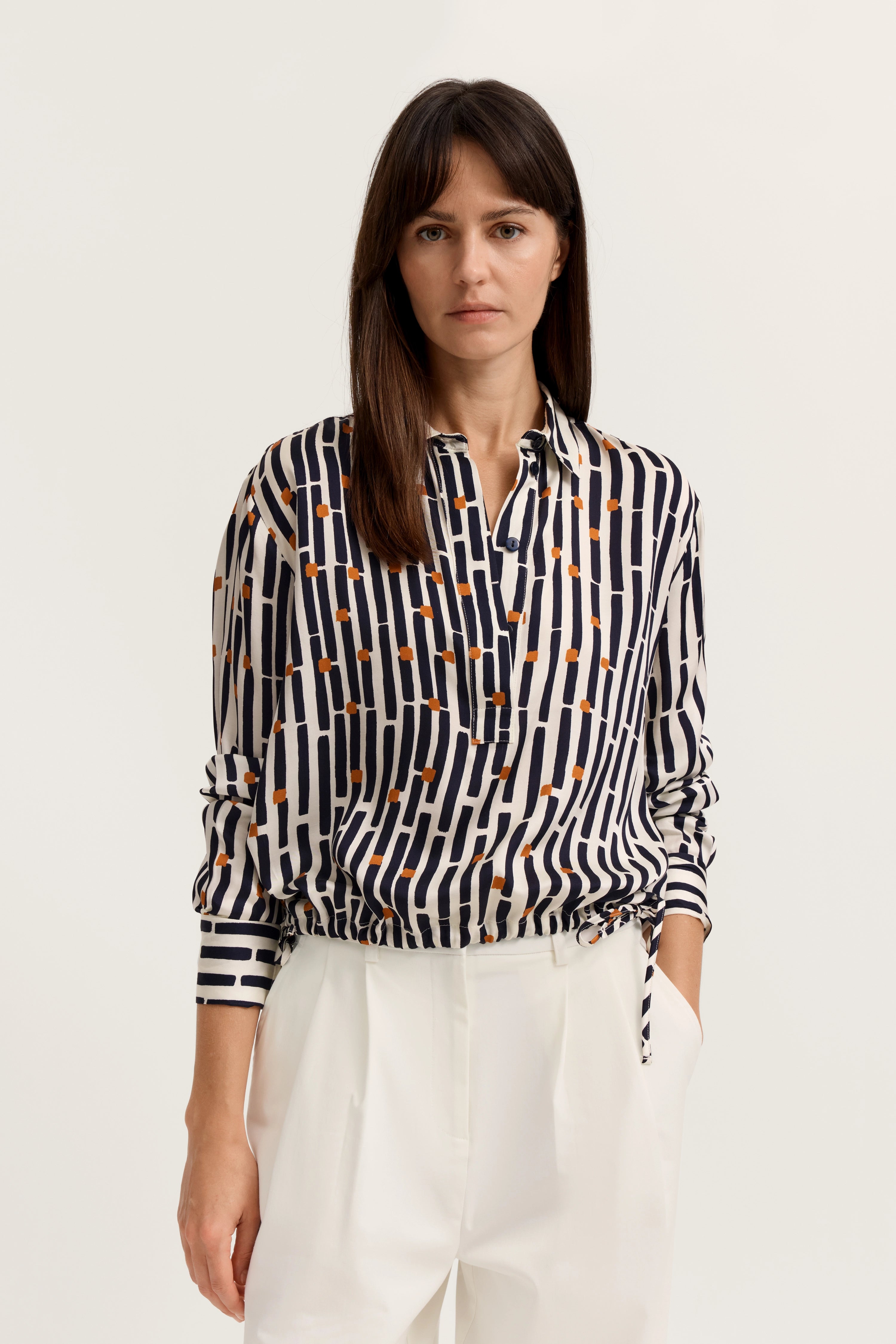 Bluse mit Streifen und Punkten in Blau-Orange, weißer Hintergrund, Model frontal, lässige Pose.