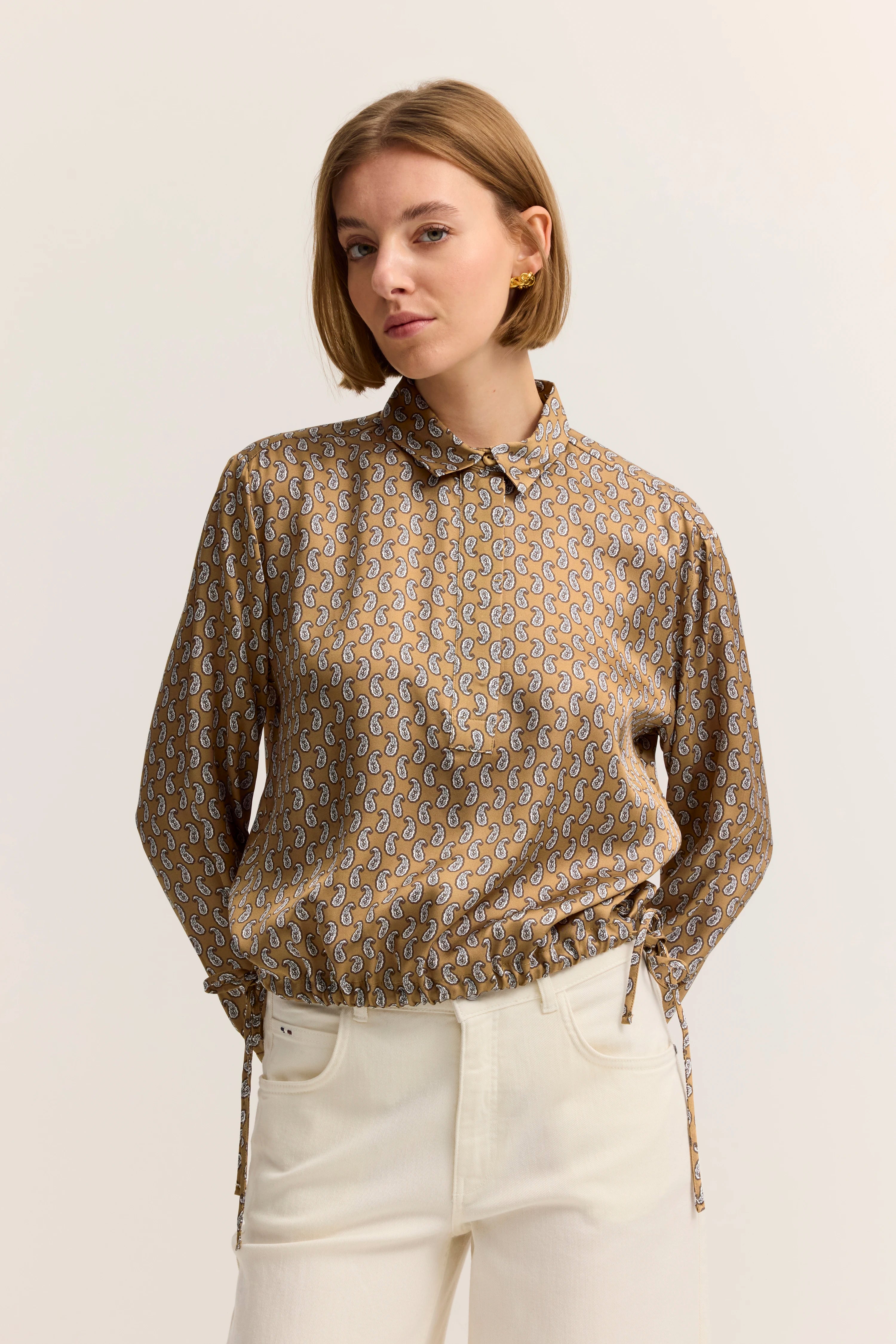 Paisley-Bluse in Beige, Modelbild mit selbstbewusstem Posing, weißer Hose, bugatti Stil.