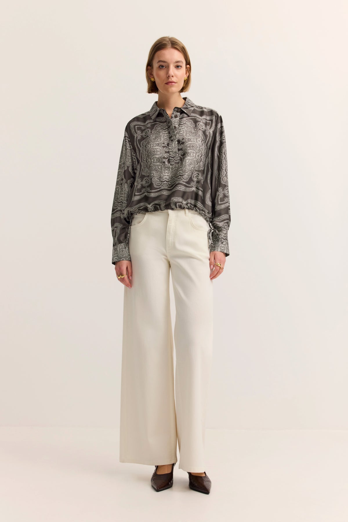 Elegantes Modelbild: Schwarz-weiß gemusterte Bluse und weiße Hose von bugatti, entspannte Pose.