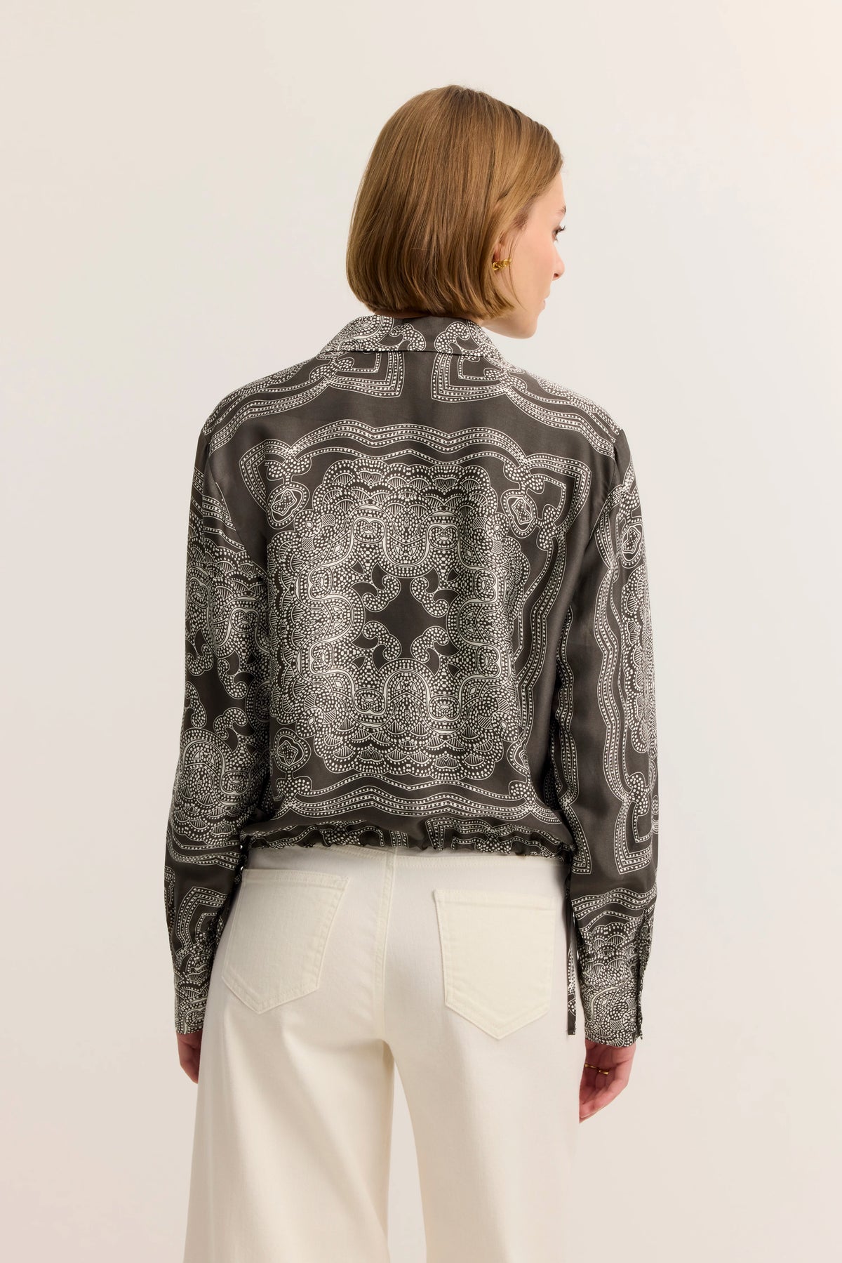 Seidenbluse mit Paisley-Muster in Dunkelgrau, kombiniert mit cremeweißer Hose, Rückansicht Model.