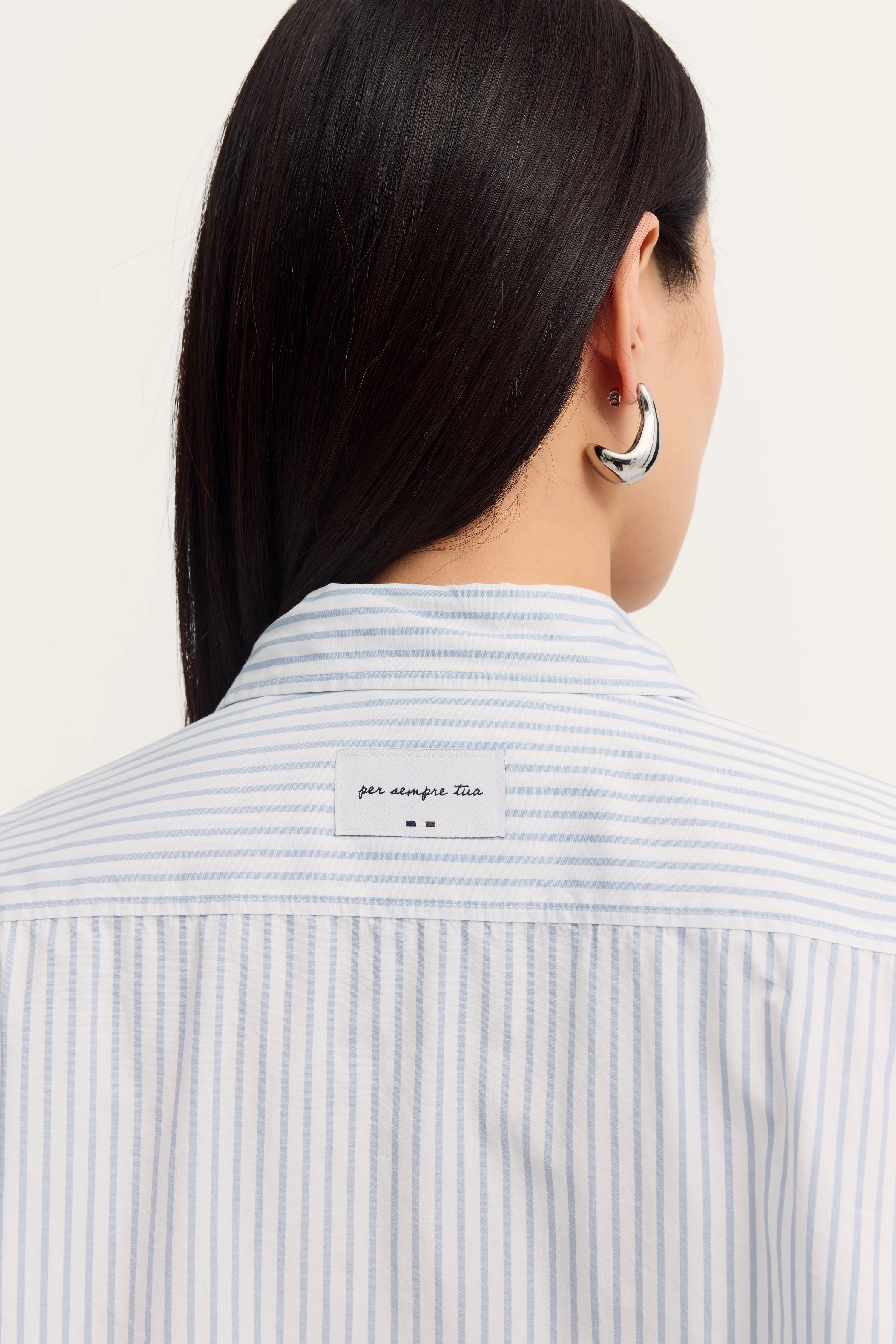 Blau-weiß gestreiftes Hemd, Rückansicht, silberner Ohrring, legeres Modelbild mit glattem Haar.