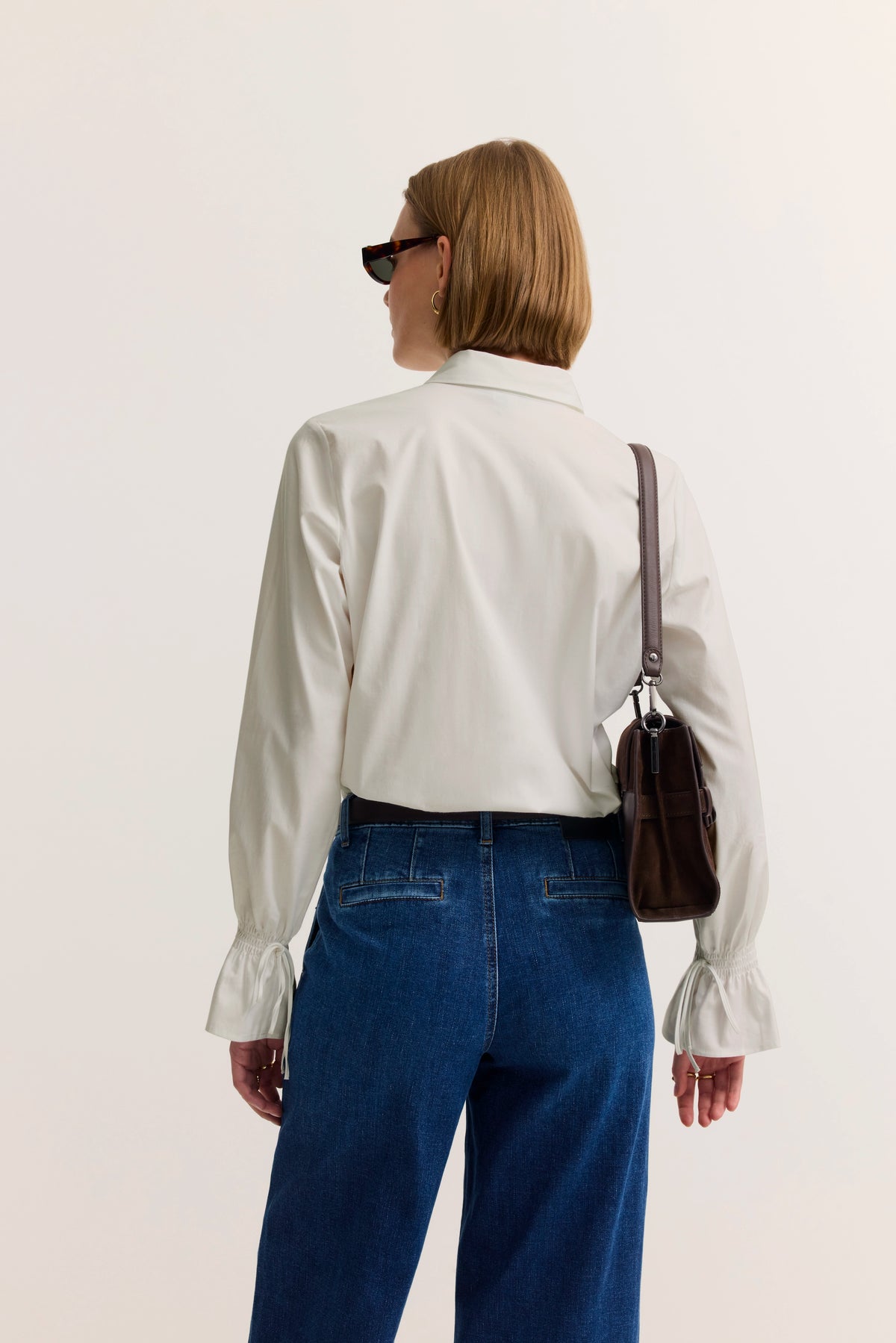 Weiße Bluse mit langen Ärmeln und blauen Jeans, Modelbild von hinten, braune Tasche.