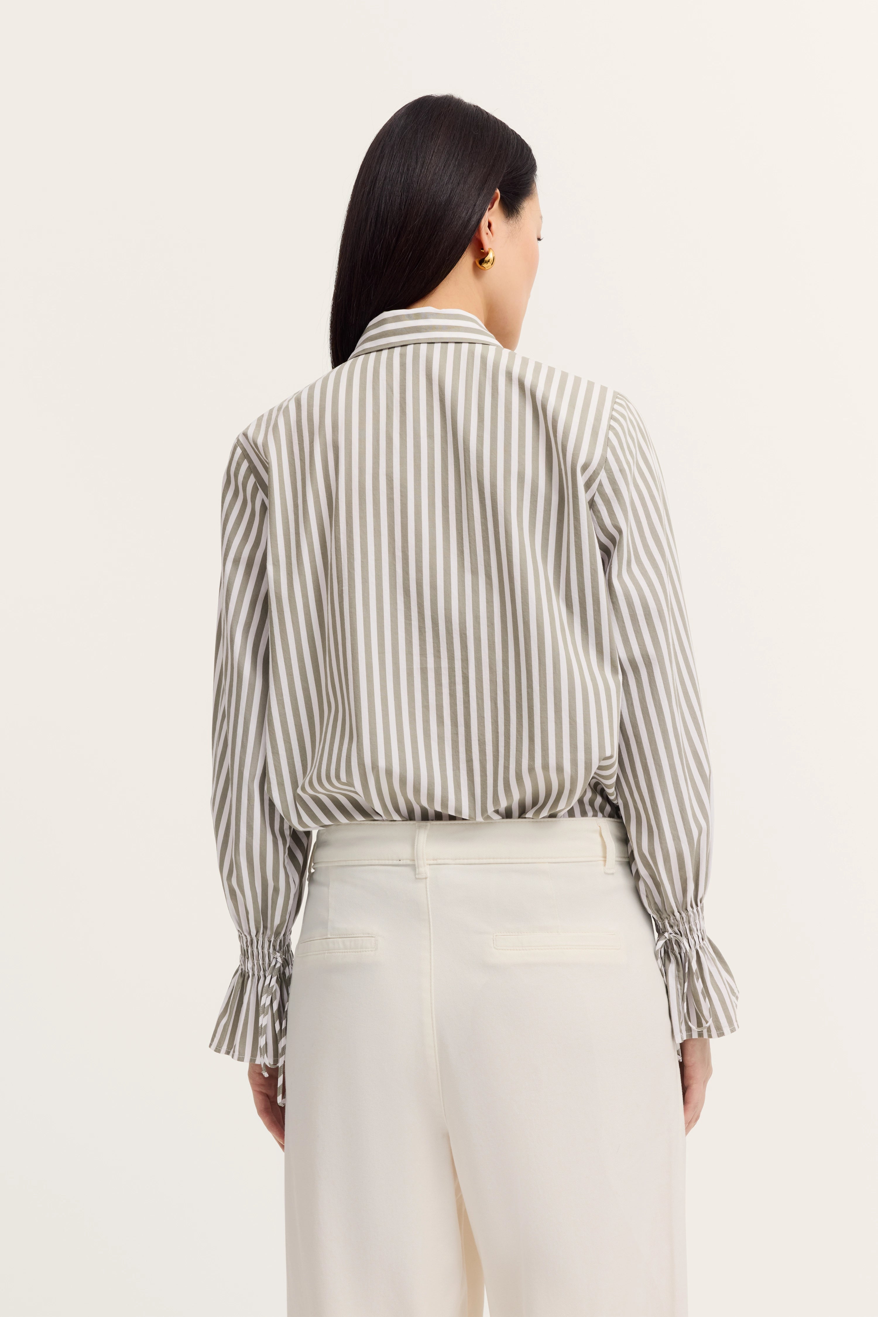 Gestreifte Bluse in Beige-Weiß, weite weiße Hose, Model von hinten, lässige Eleganz von bugatti.