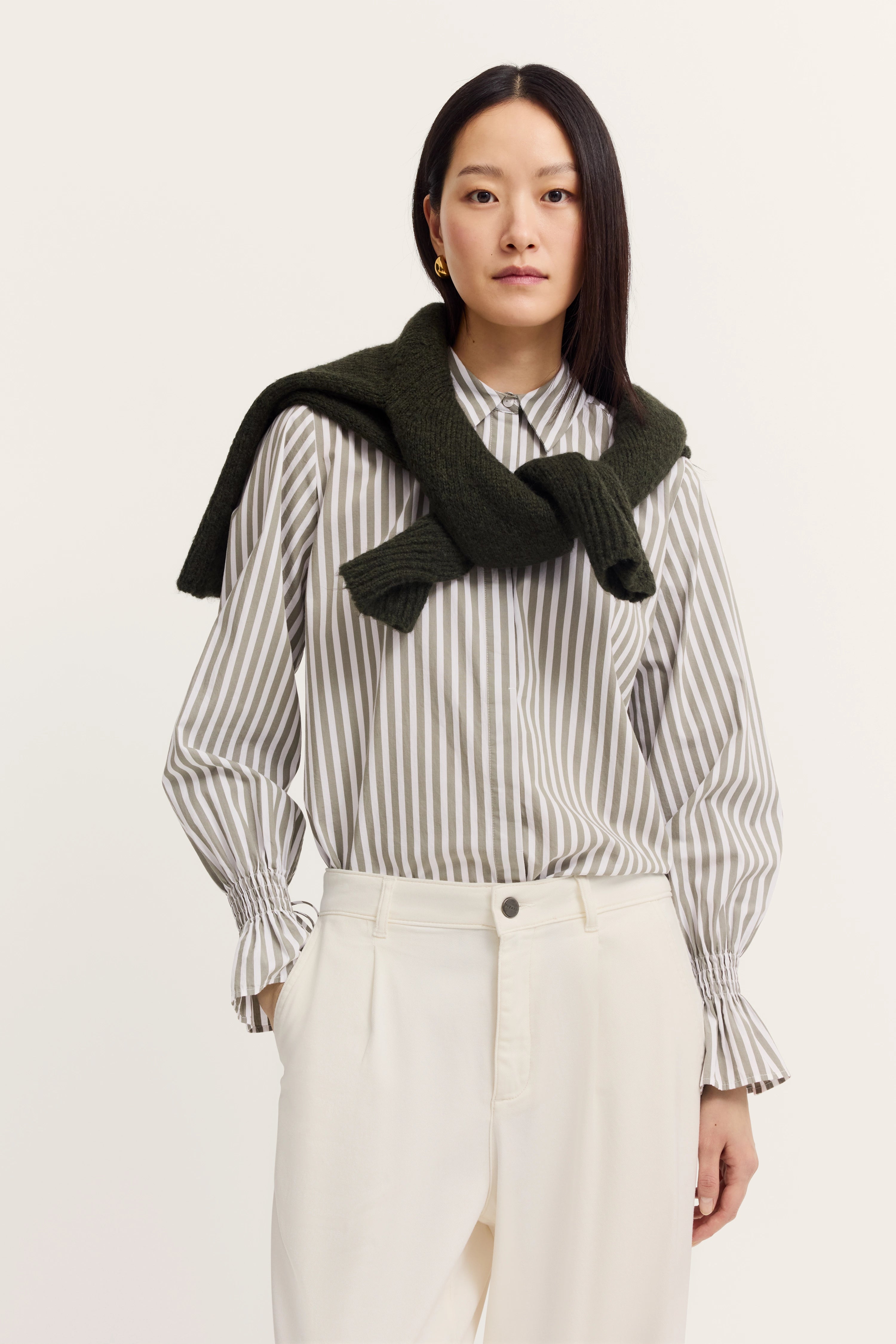 Büstenbild mit gestreiftem Hemd in Beige-Weiß, dunkelgrüner Pullover über den Schultern.