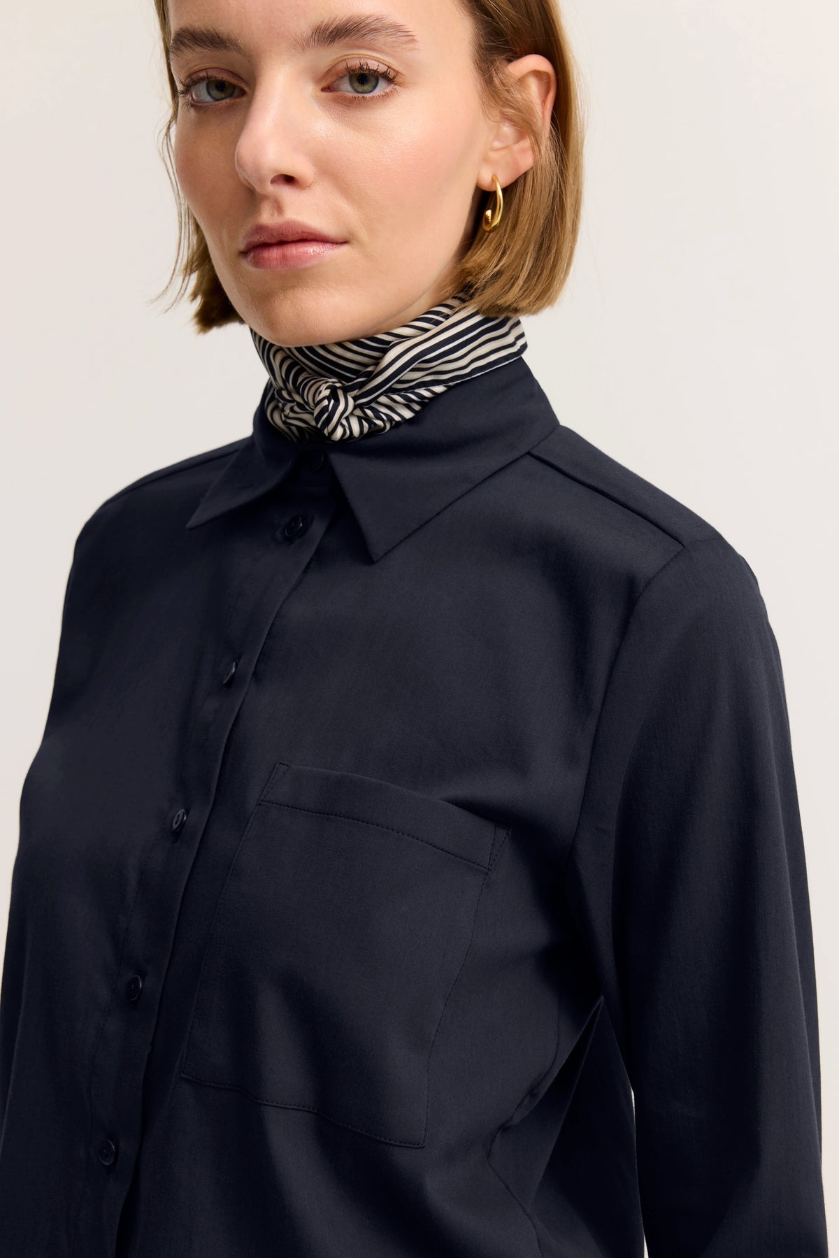 Rückansicht: Model in navy Bluse und weißen Jeans, leger stehend.