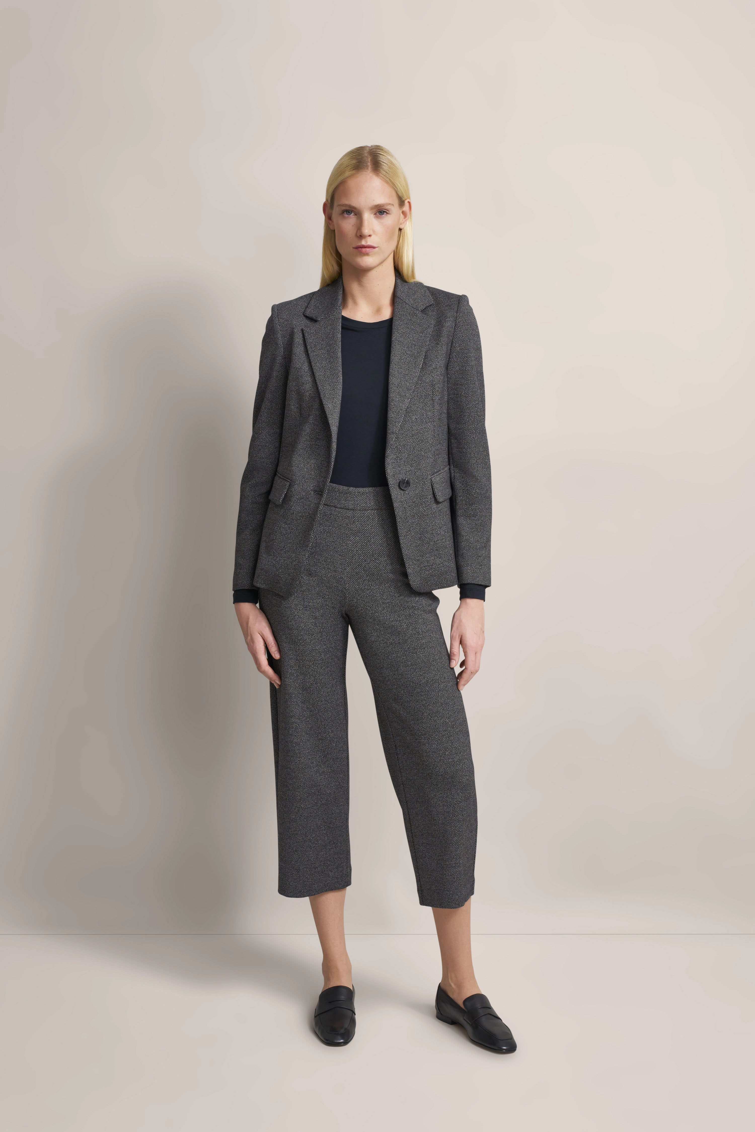 Model in gray pantsuit with blazer, black top, relaxed pose, bugatti style and elegance.