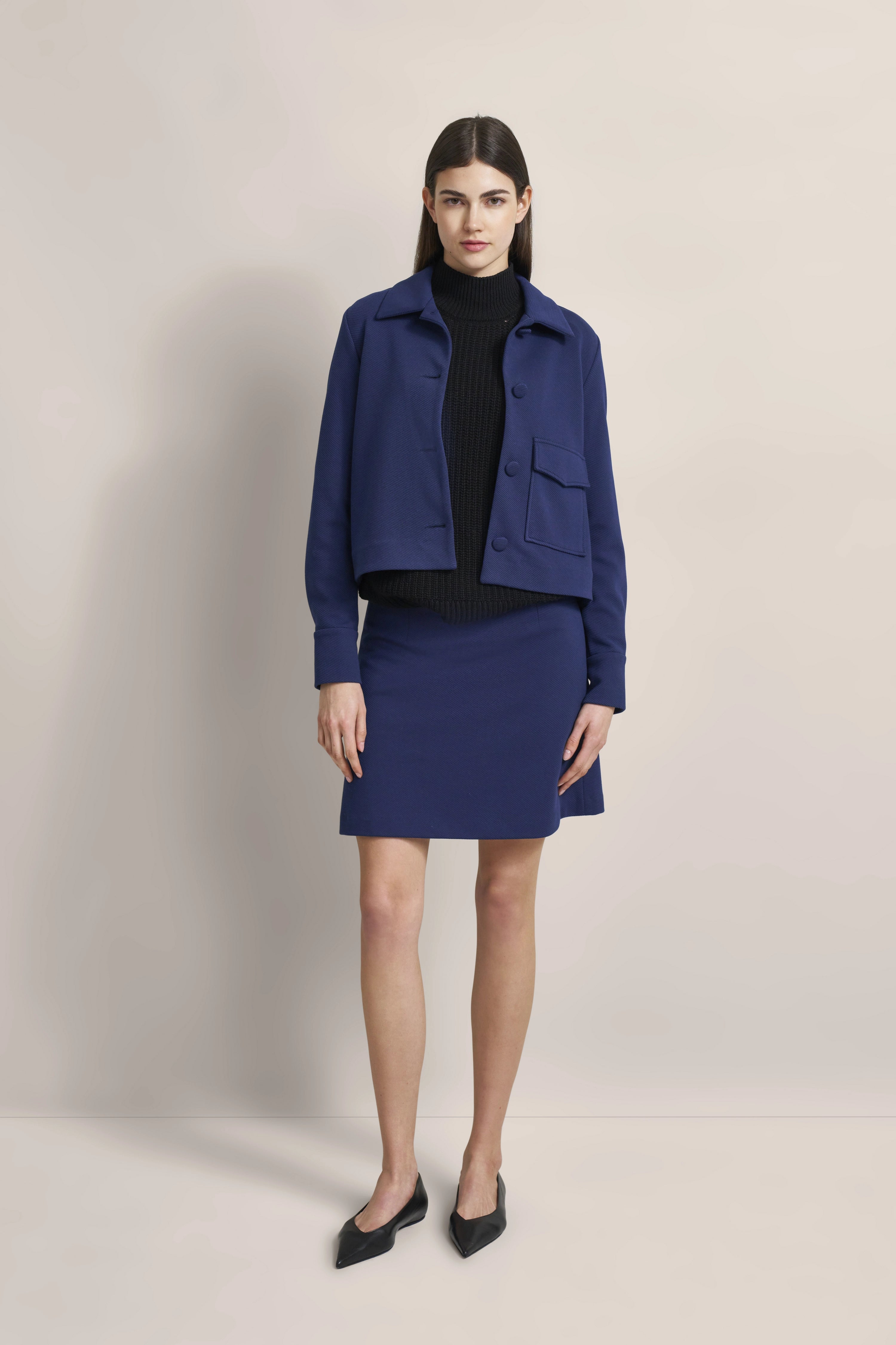 Model in marineblauem bugatti Rock und Jacke, schwarzer Rollkragen, elegante Pose.