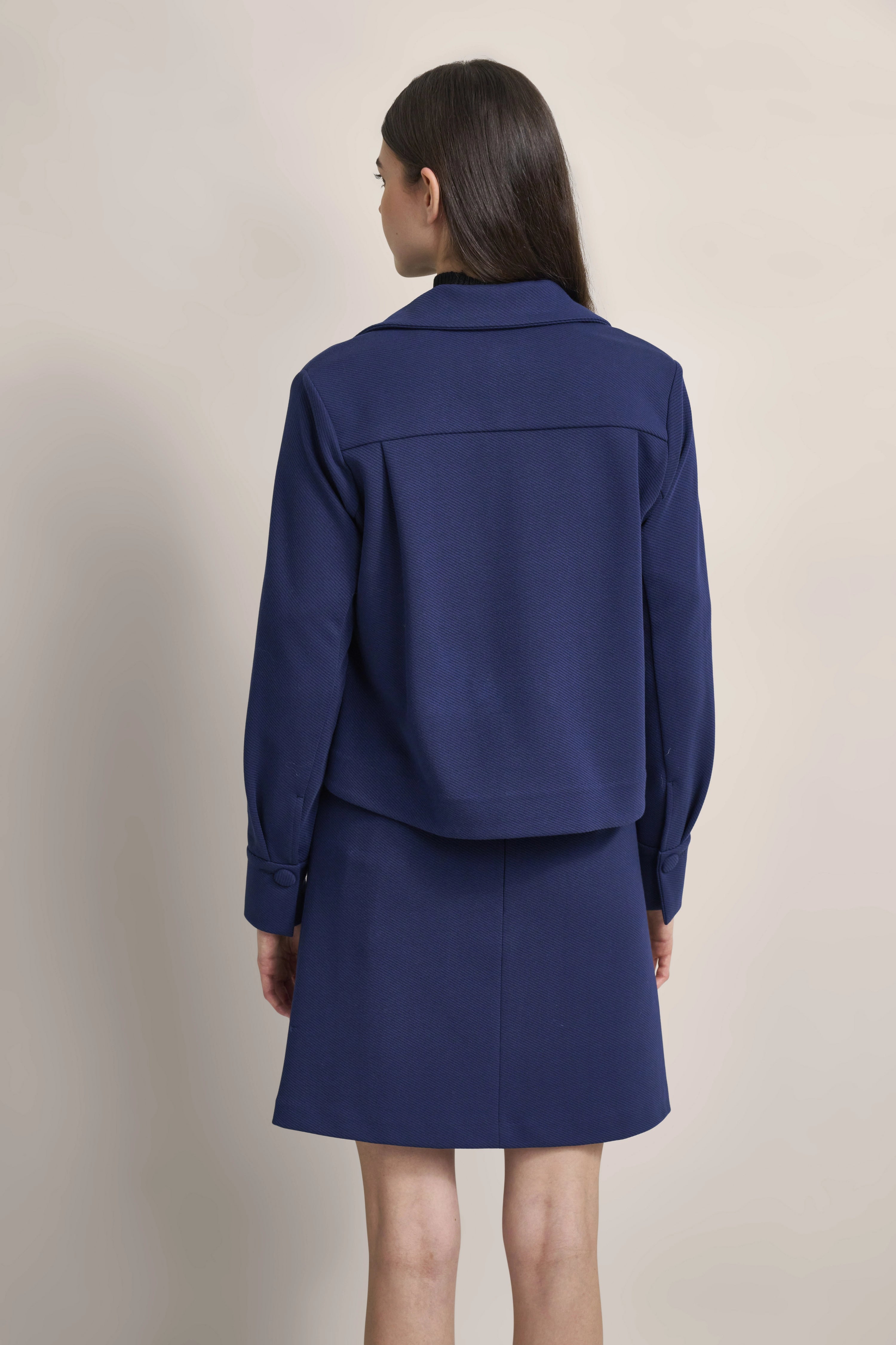 Model in blauer Jacke und Rock von bugatti, Rückansicht, legeres Outfit, schlichtes Design.