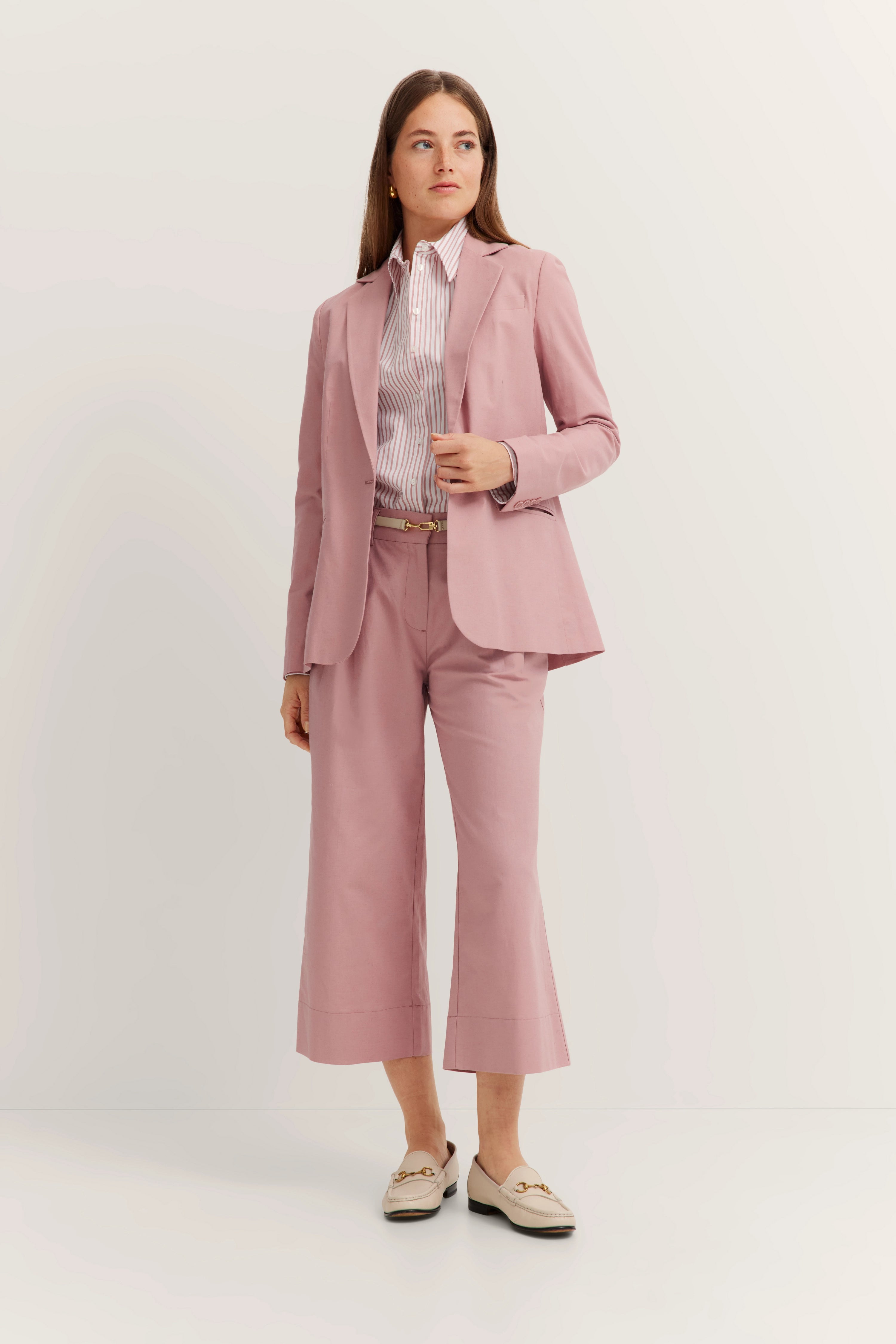 Model in rosa bugatti Anzug mit Streifenhemd, leger posiert, Hände in Hosentasche, elegante Loafer.