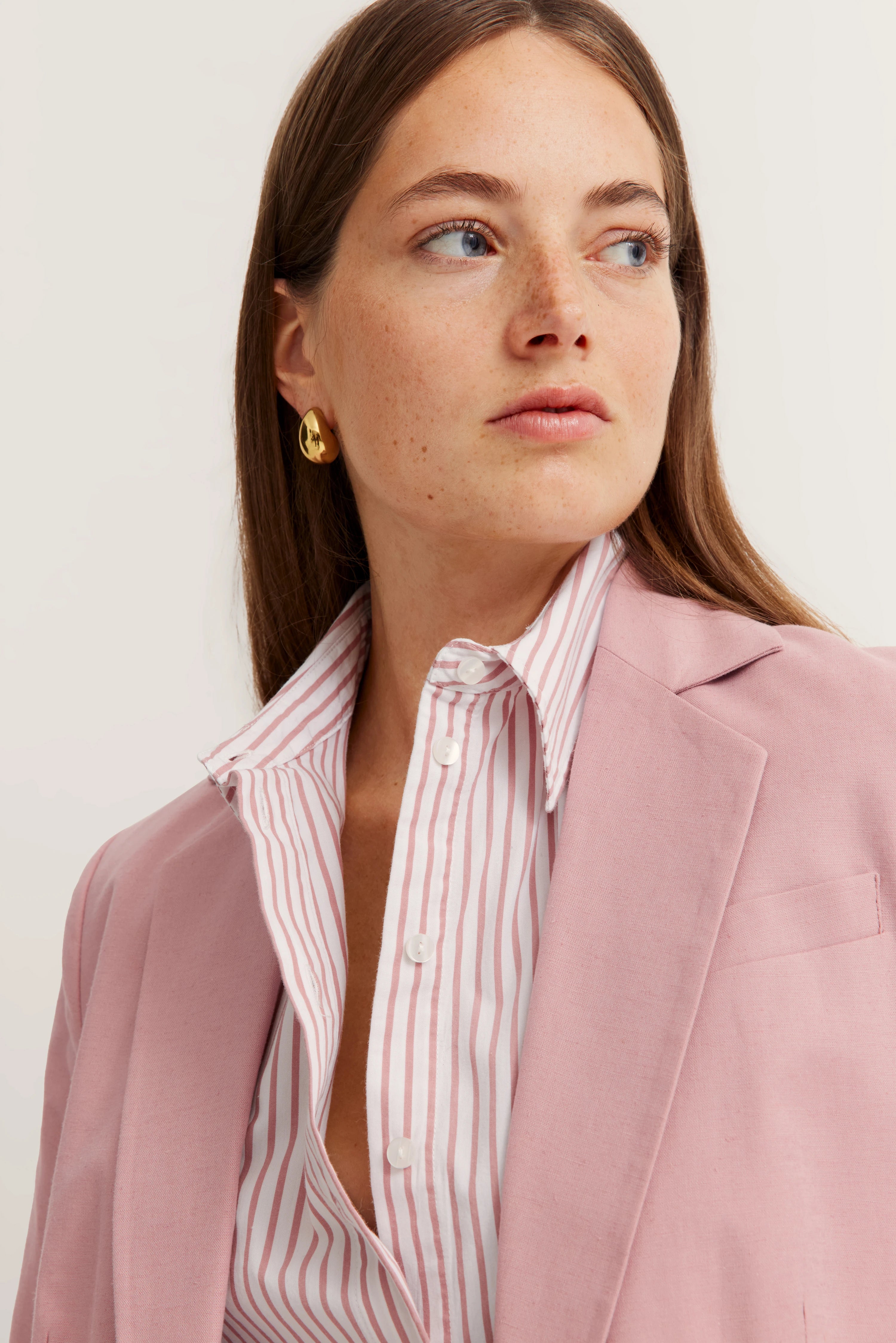 Modelbild mit rosa bugatti Blazer, gestreiftem Hemd in Weiß und Rosa, goldene Ohrringe, elegantes Posing.