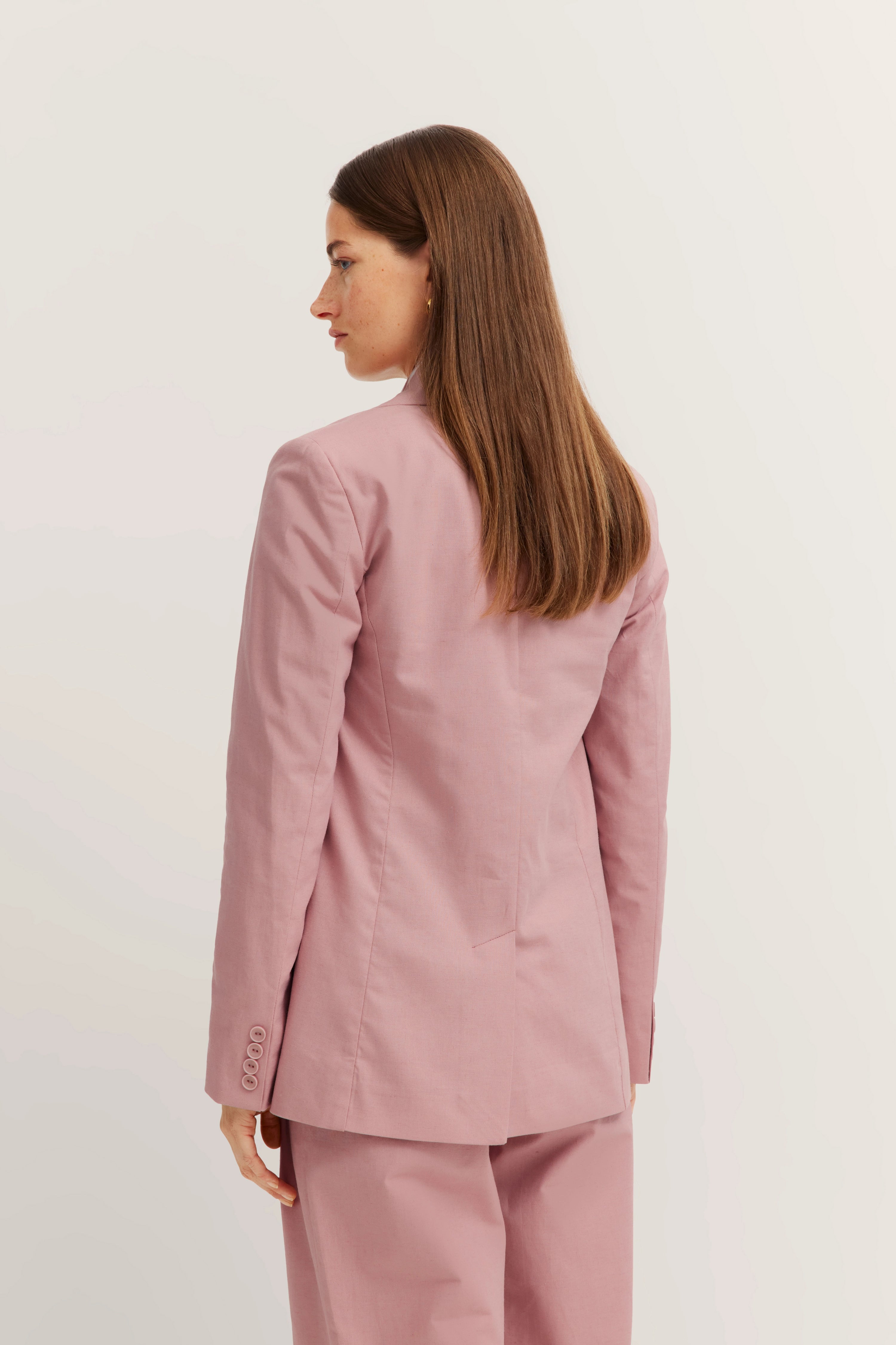 Achteraanzicht model in roze bugatti pak, ontspannen pose, elegante, tijdloze stijl.