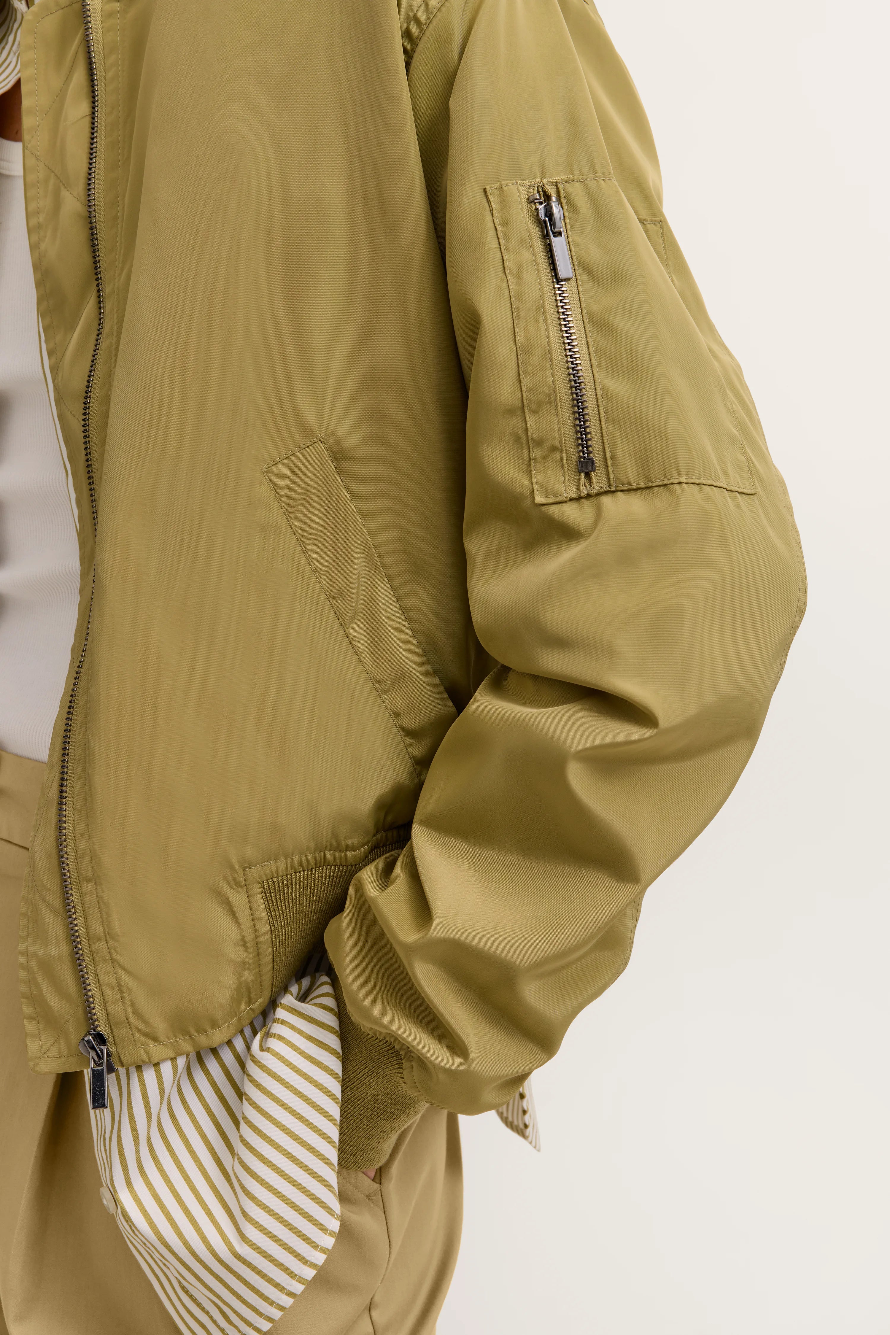 Khakifarbene Bomberjacke von bugatti, Detailansicht mit Reißverschluss und gestreiftem Innenfutter.