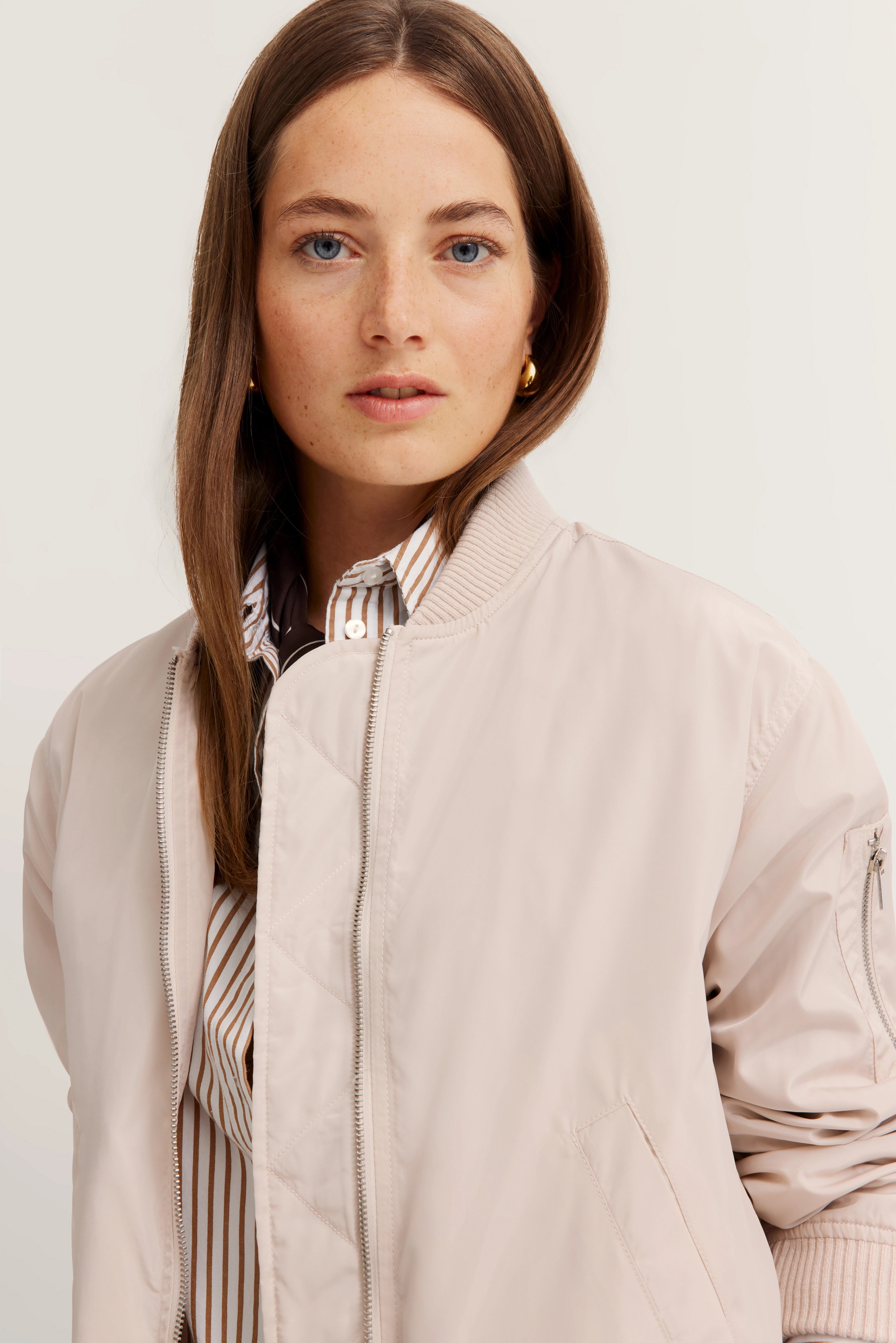 Büste in beige Bomberjacke, gestreifte Bluse, lässiger bugatti Stil.