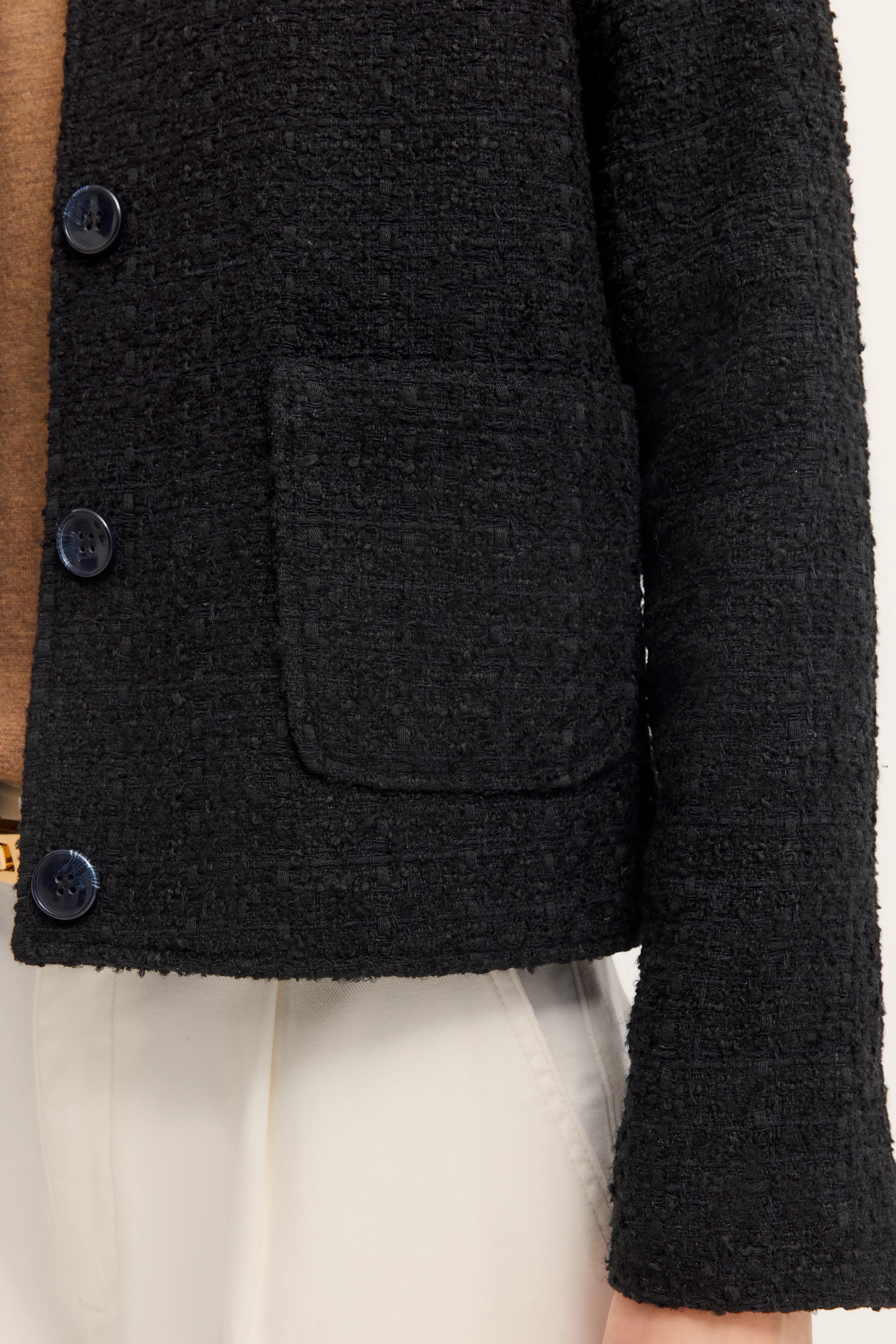 Schwarze bouclé Jacke, brauner Pulli, weiße Hose, Büstenbild, elegante Textur und Details.