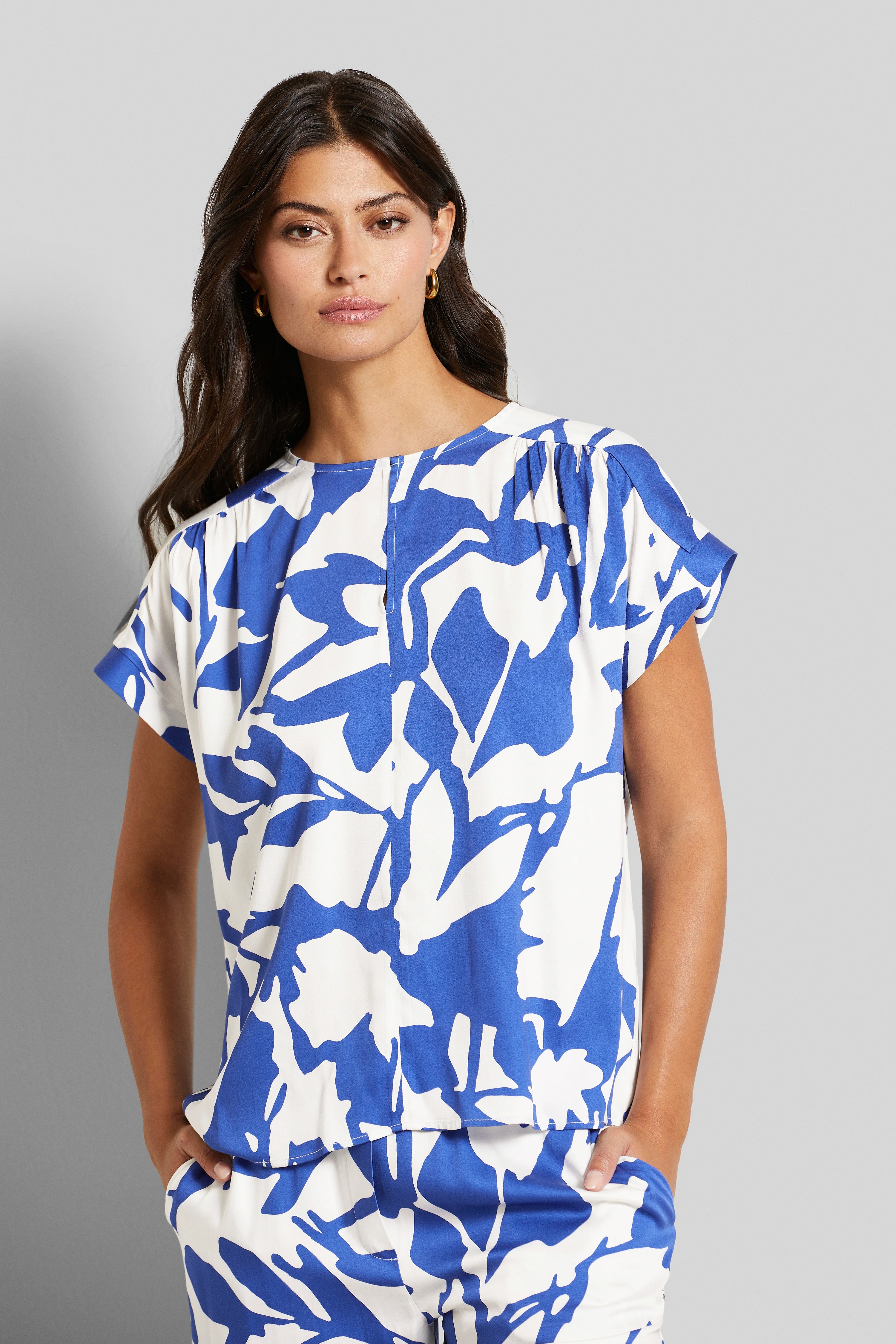 Blau-weißes Muster-Outfit, Kurzarmbluse und Hose, Modelbild mit entspannter Pose.