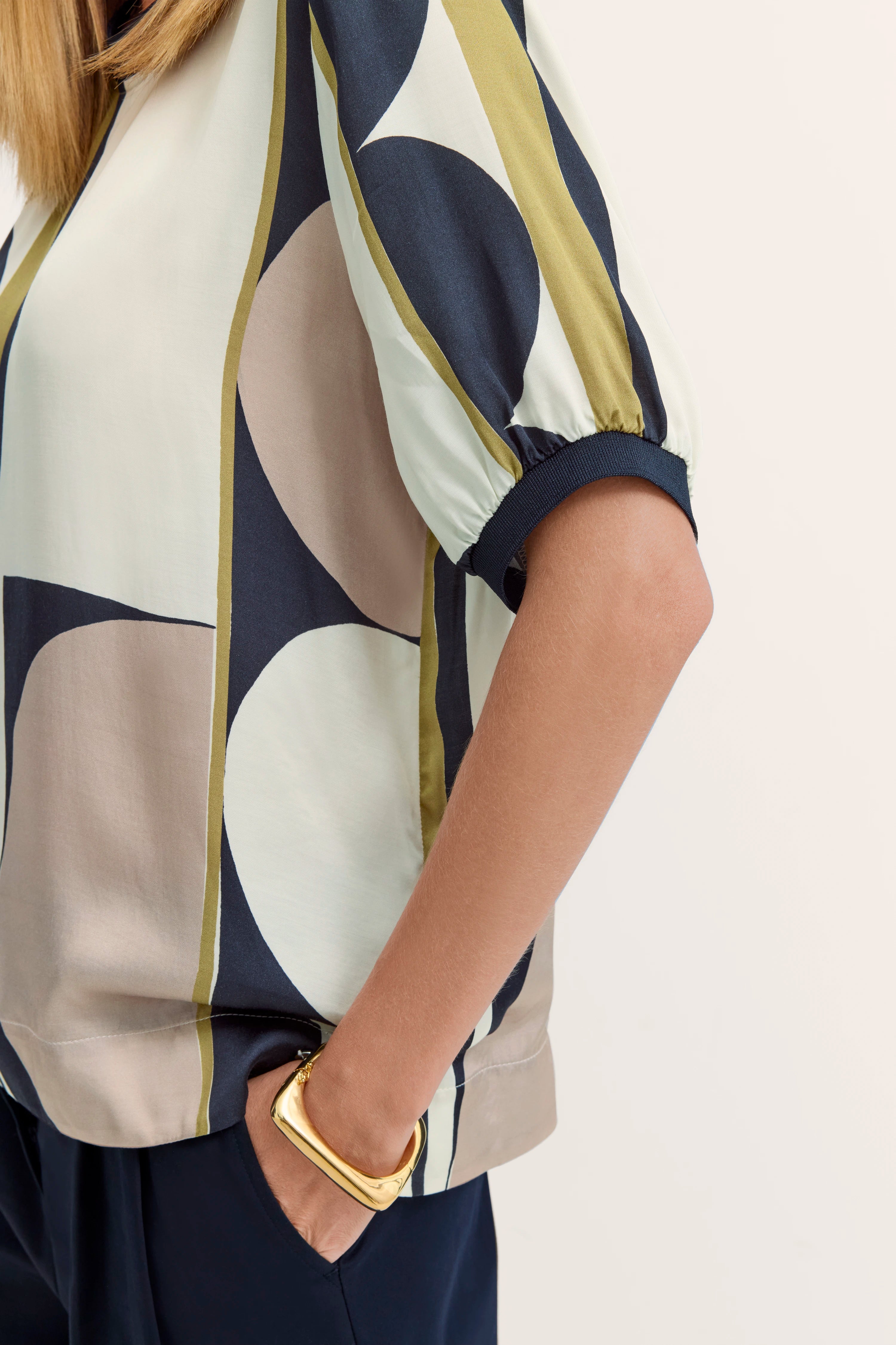 Bluse mit geometrischem Muster in Blau, Beige und Oliv, getragen von Model in legerer Pose, bugatti Stil.