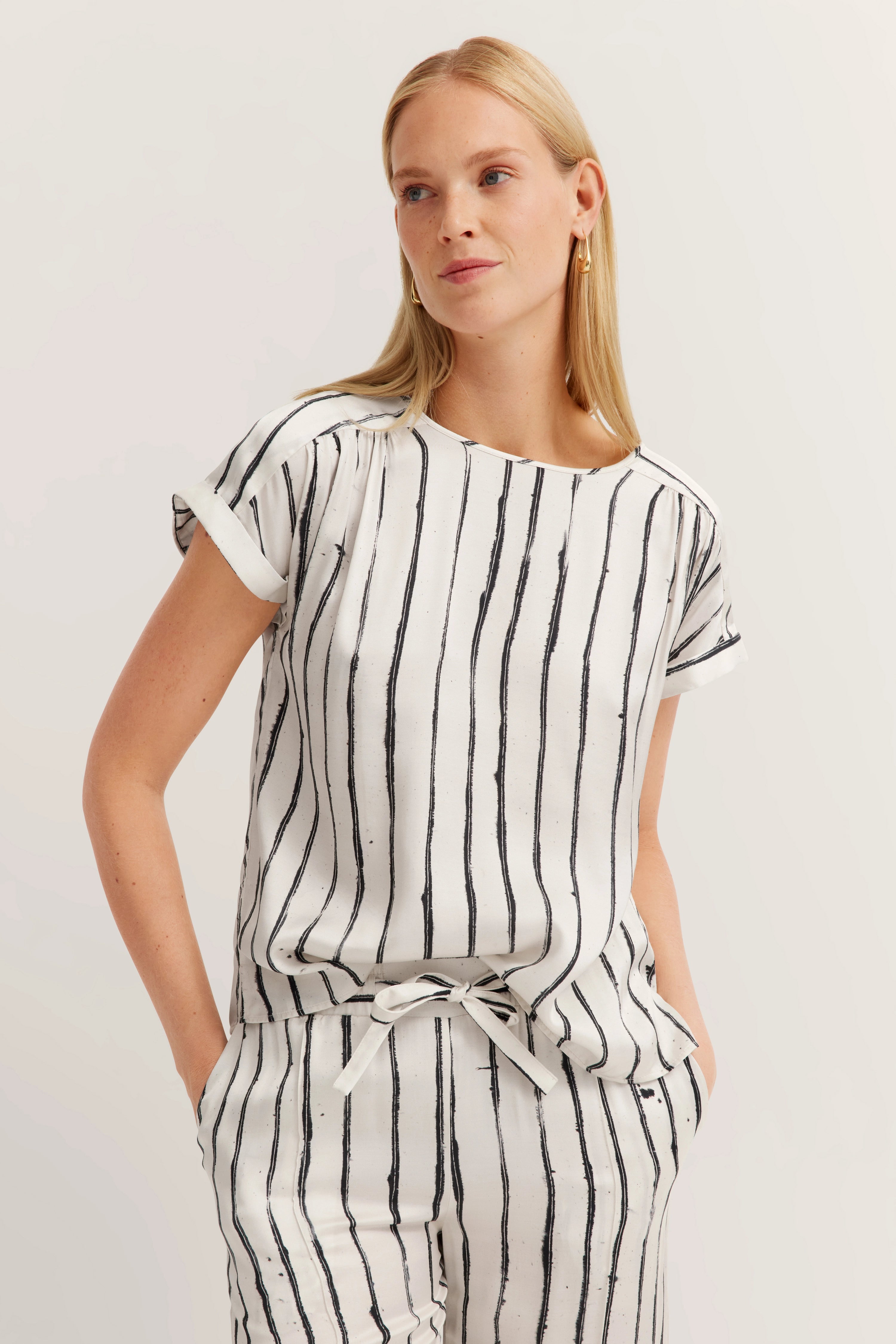 Weiße gestreifte Bluse und Hose, Modelbild, lässig mit Händen in den Taschen.