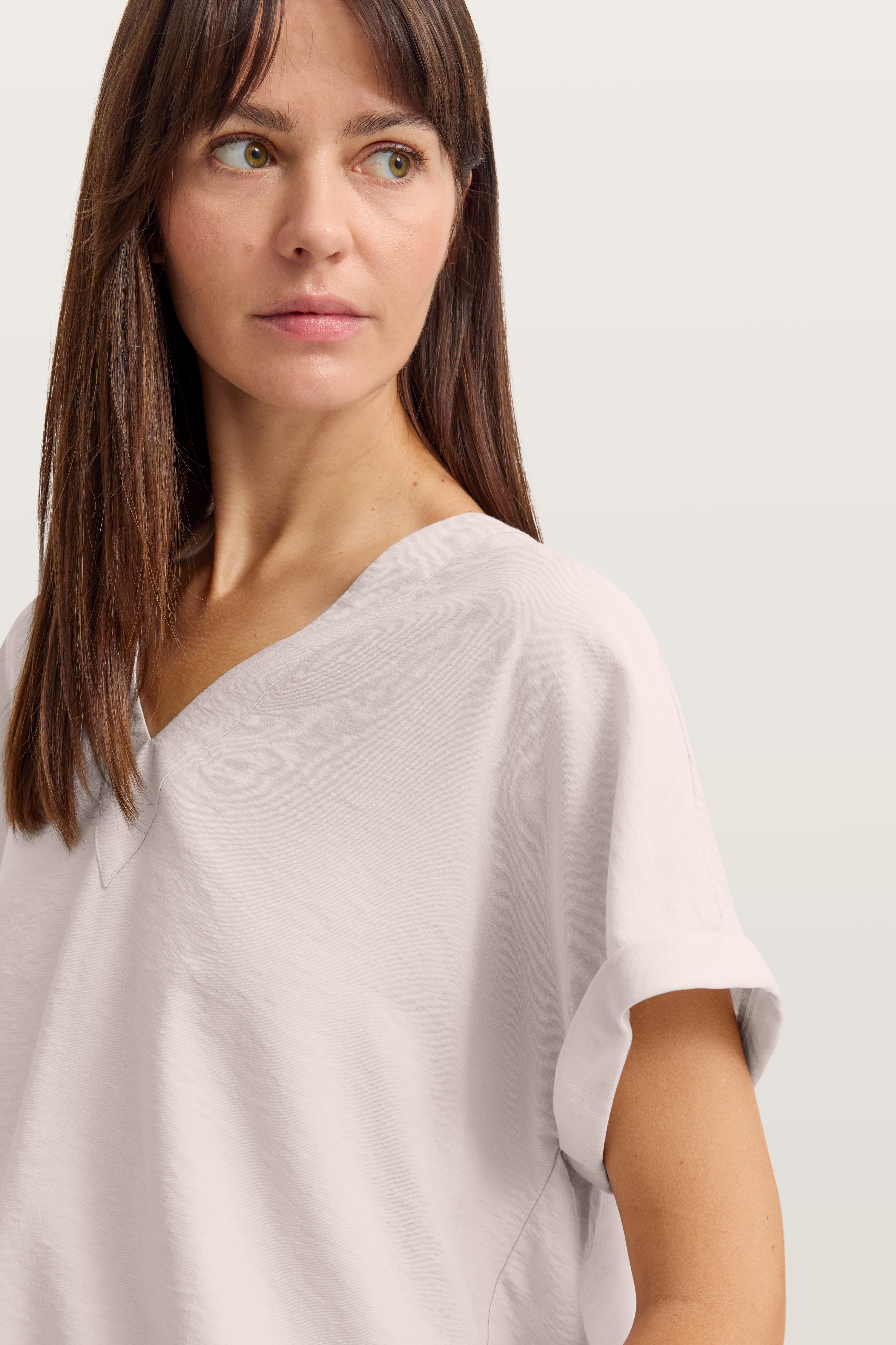 Rückenansicht Model in beigefarbenem T-Shirt und heller Hose, legeres Posing.
