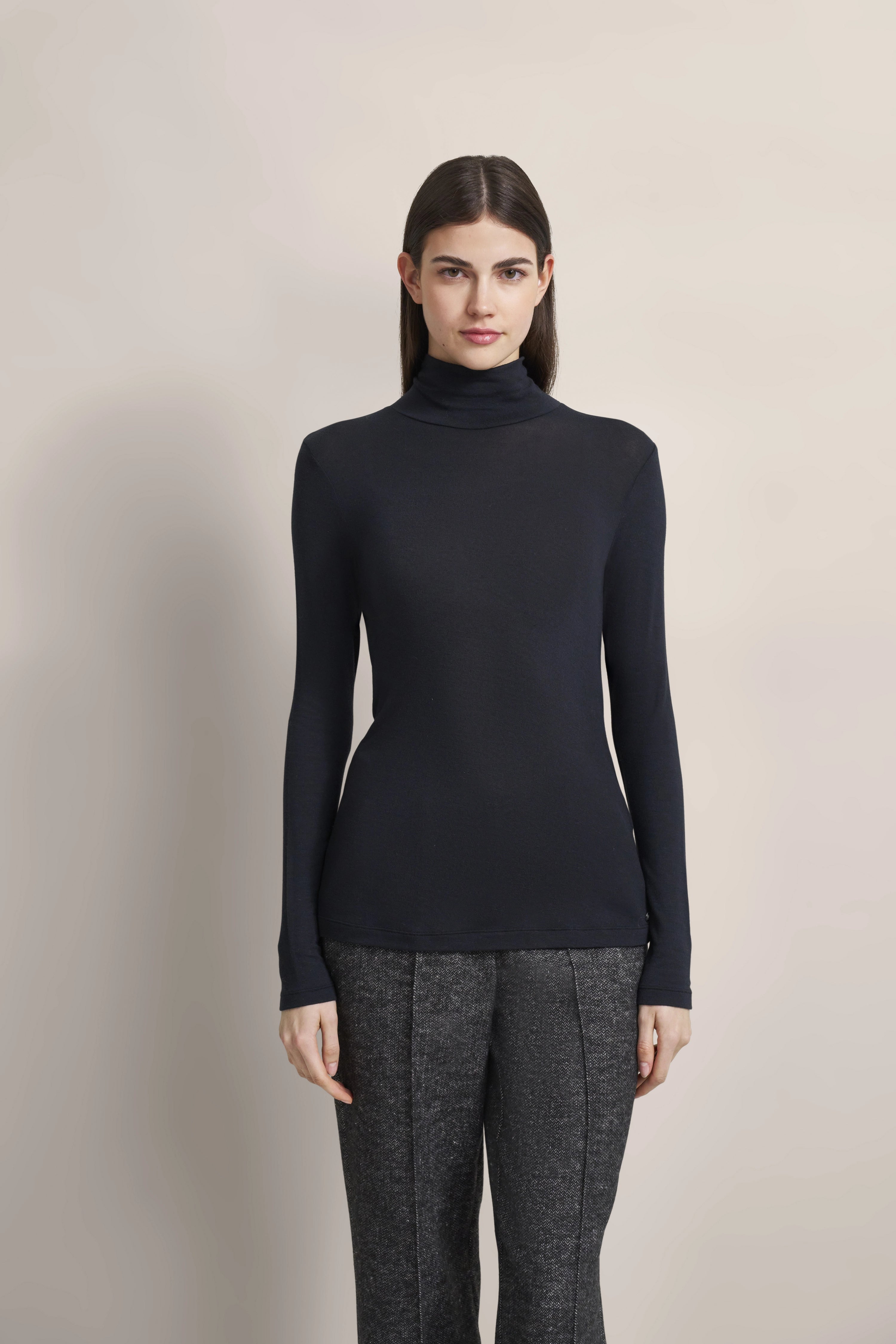 Dark turtleneck sweater and gray pants, model facing forward, relaxed pose.