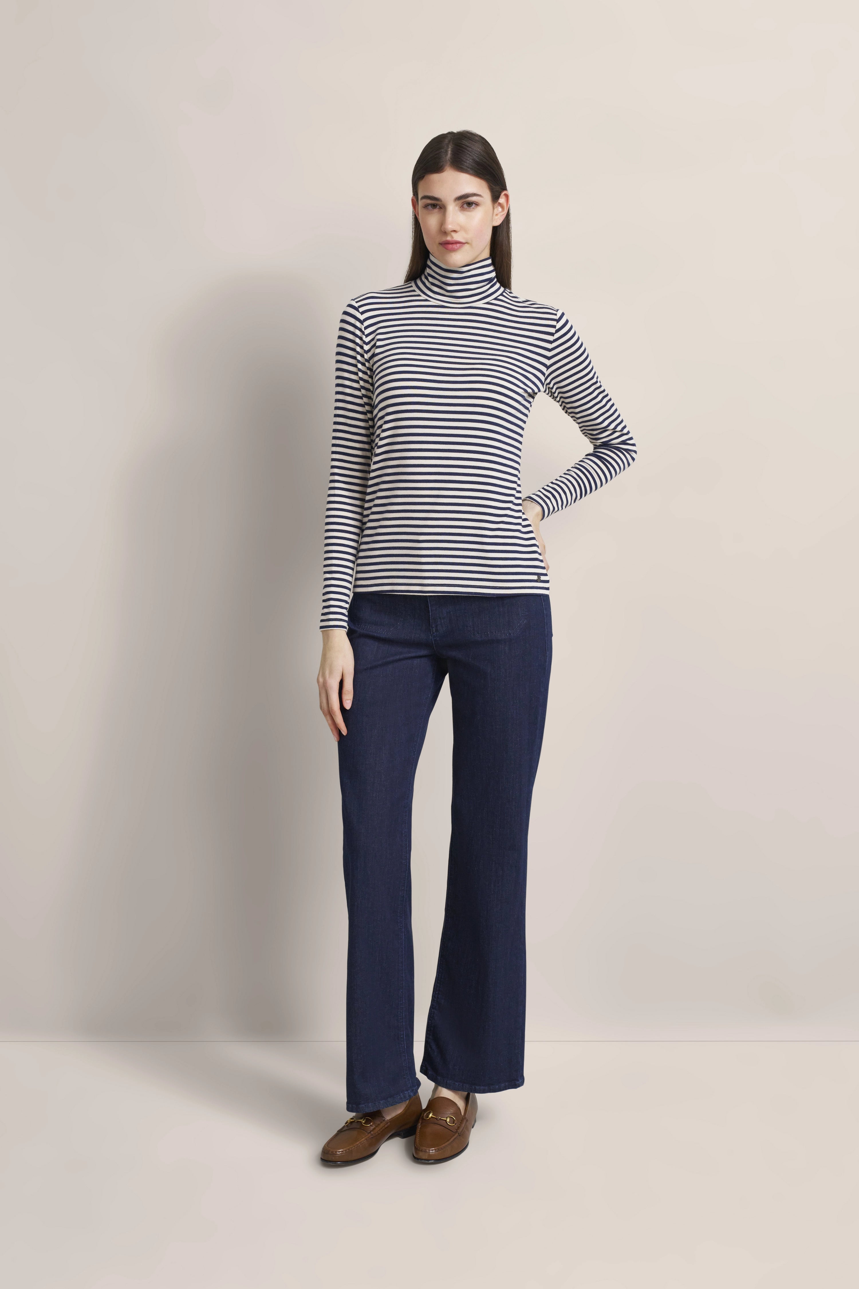 Gestreiftes Rollkragen-Top, dunkelblaue Jeans, braune Loafer, Model steht entspannt.