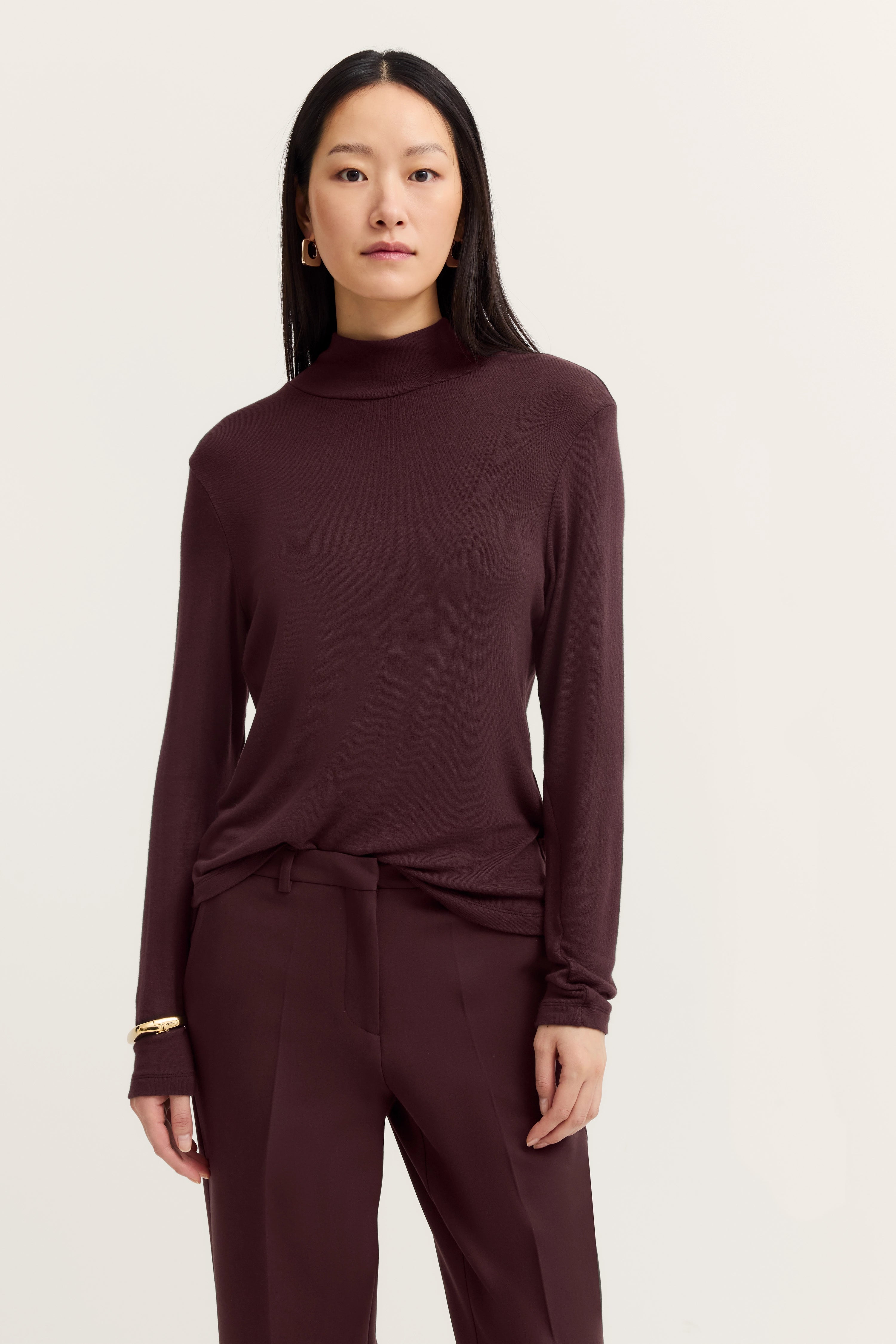 Modelbild: Frau in burgunderfarbenem bugatti Outfit mit Langarmshirt und Hose, entspannt stehend.